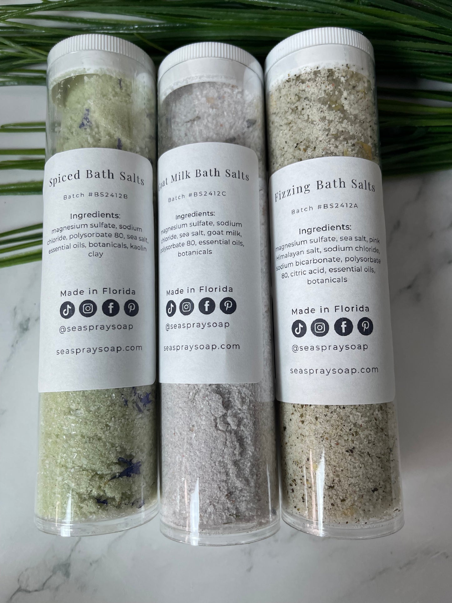 Three tubes of milk bath salts on a marble surface with a green leaf.