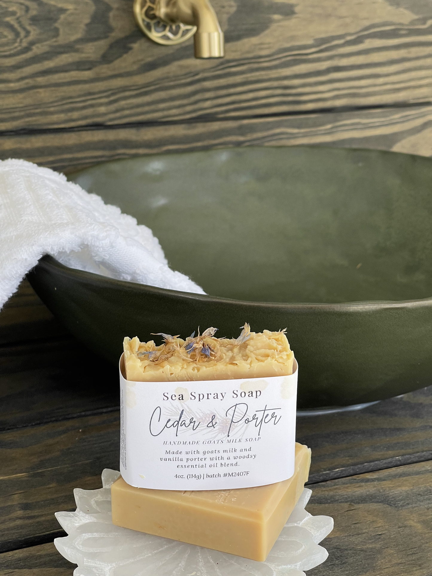 Bar of soap with a label on a wooden surface in front of a green ceramic bowl.