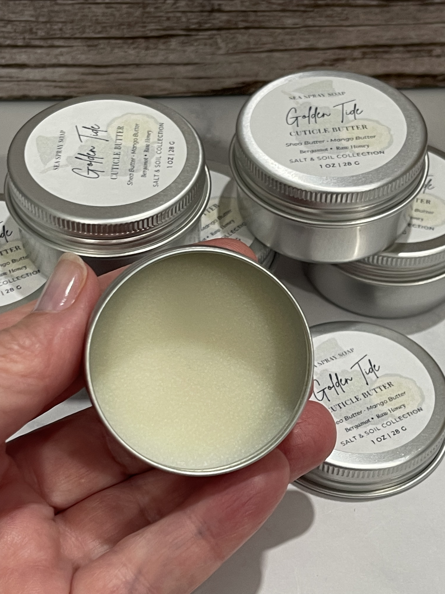 Hand holding an open tin of Golden Tole leather butter with more tins in the background.
