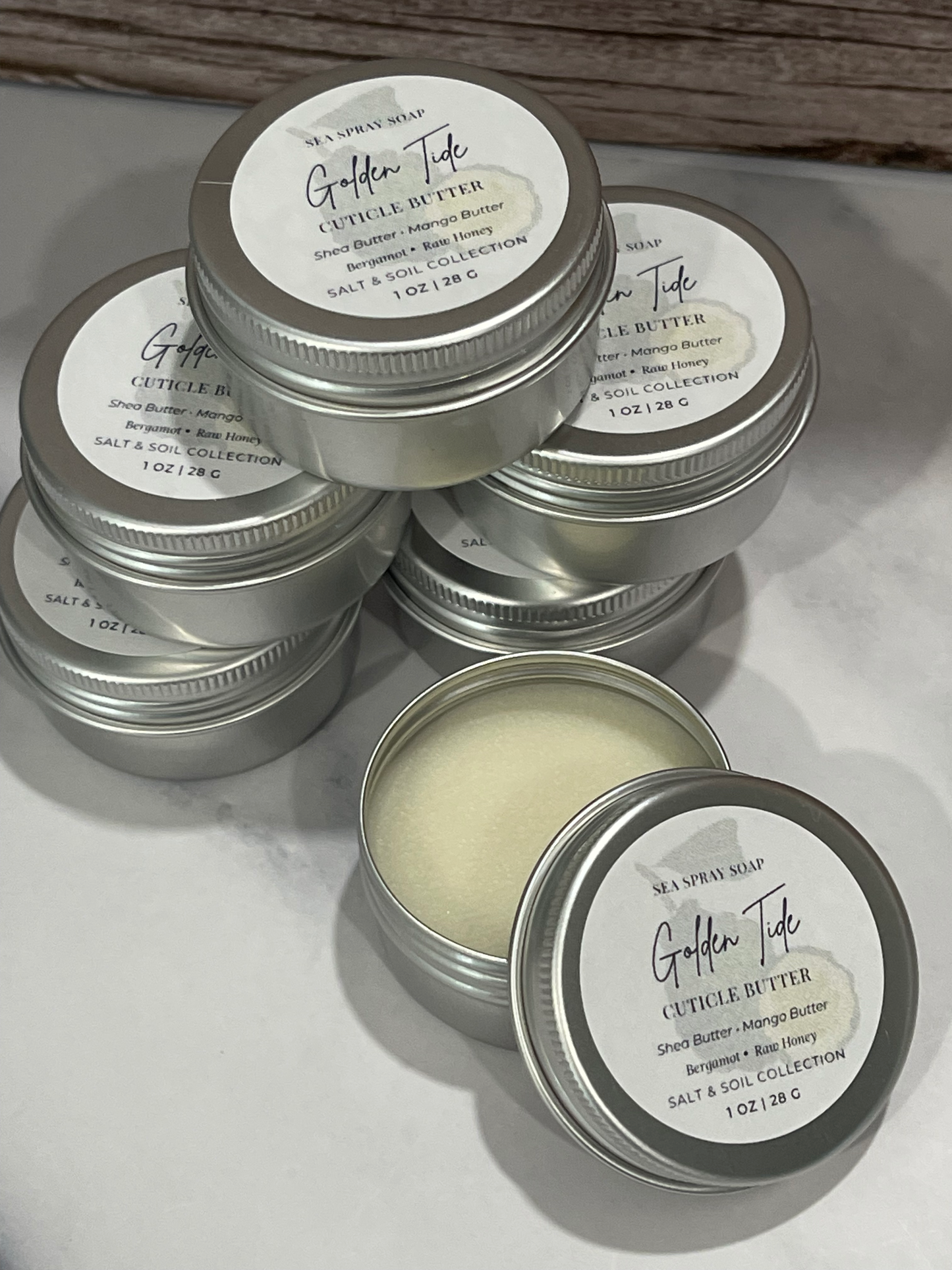 Silver tins of Golden Tide cuticle butter on a light background