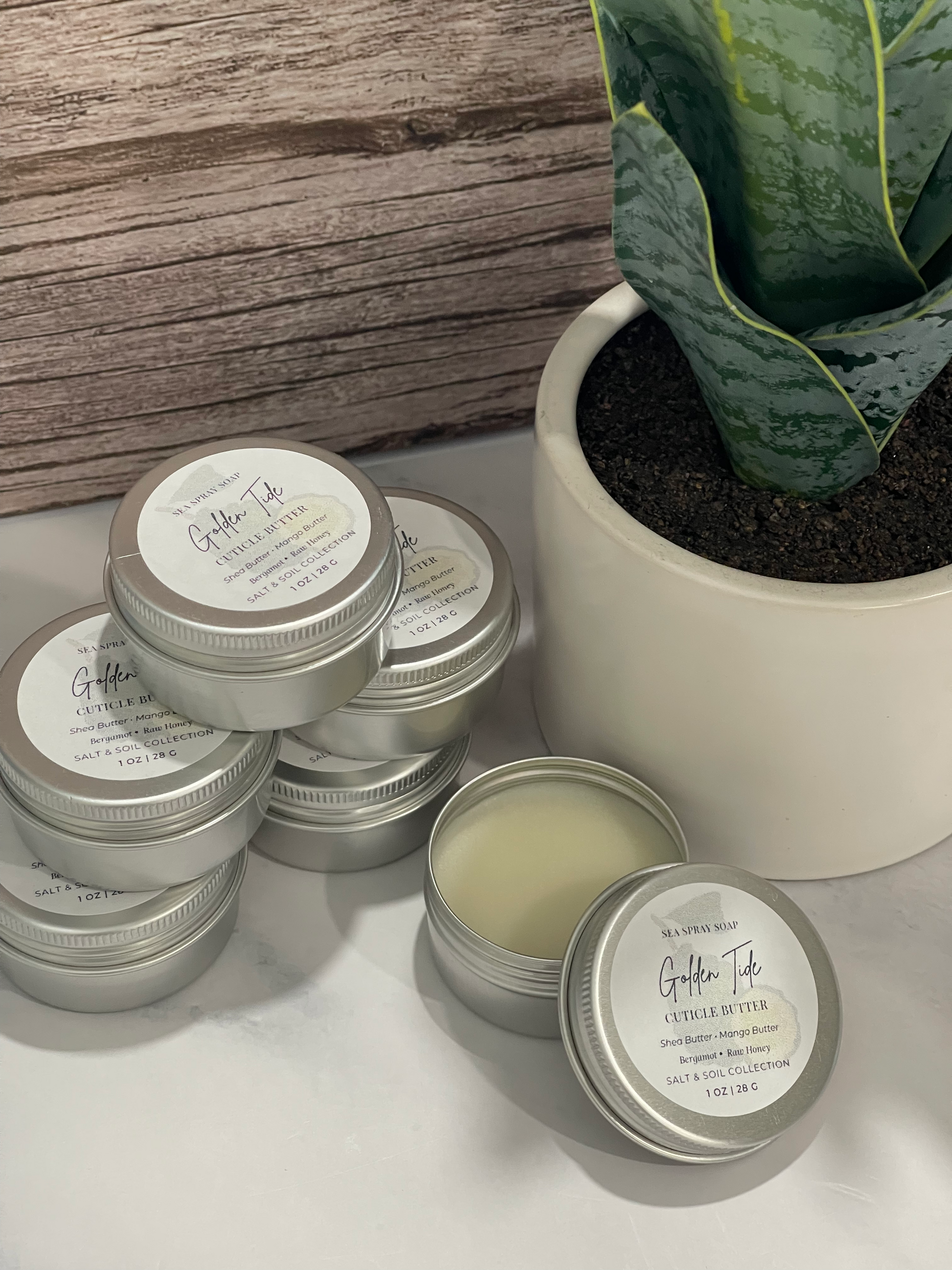 Silver tins with labels on a white surface next to a potted plant