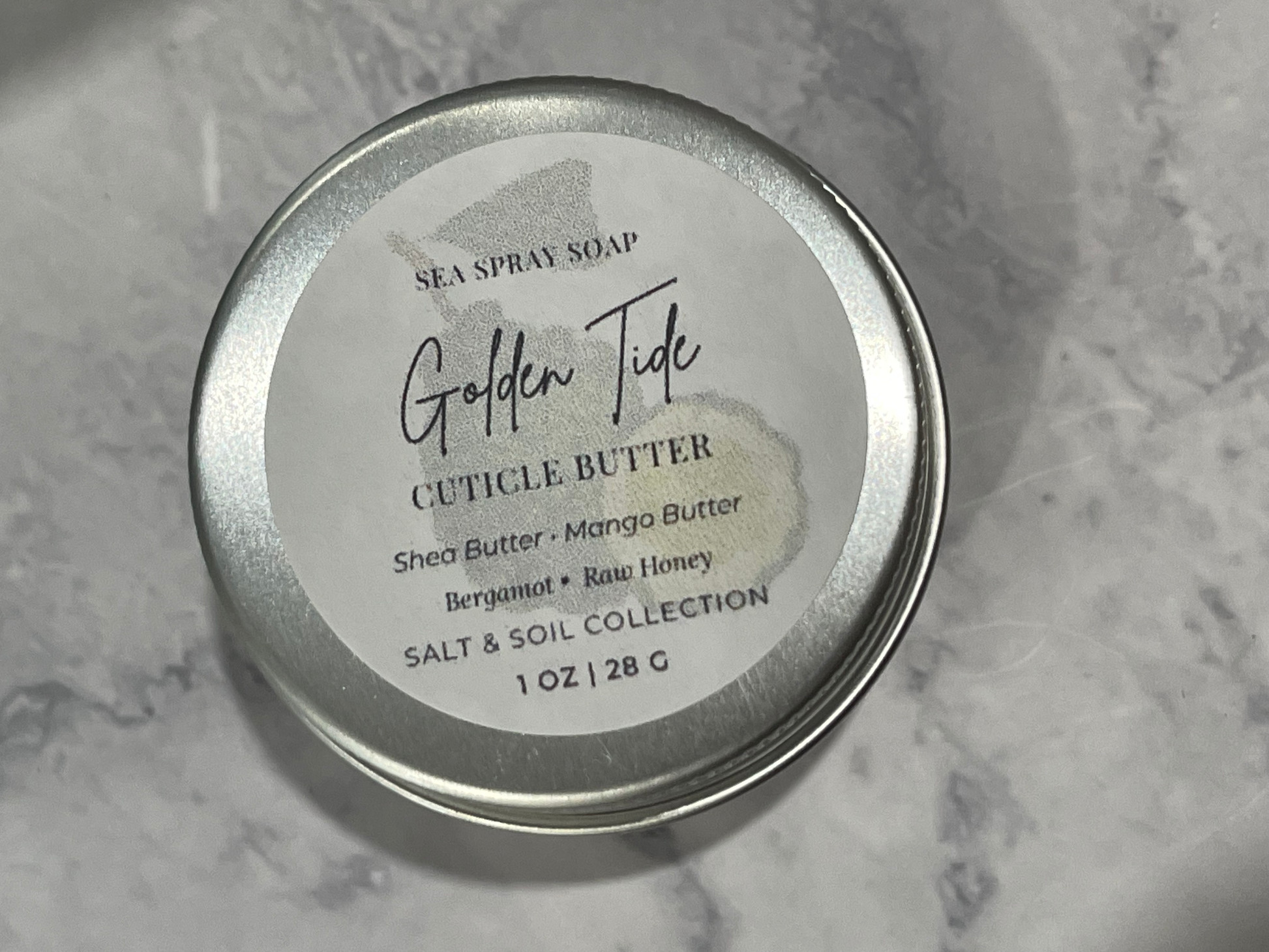 Tin of Golden Tide cuticle butter on a marble surface