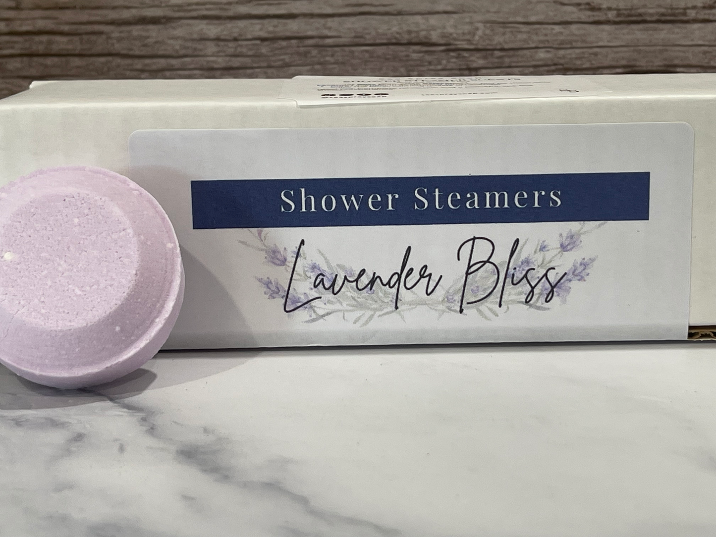 Lavender Bliss shower steamers packaging on a marble surface with a wooden background