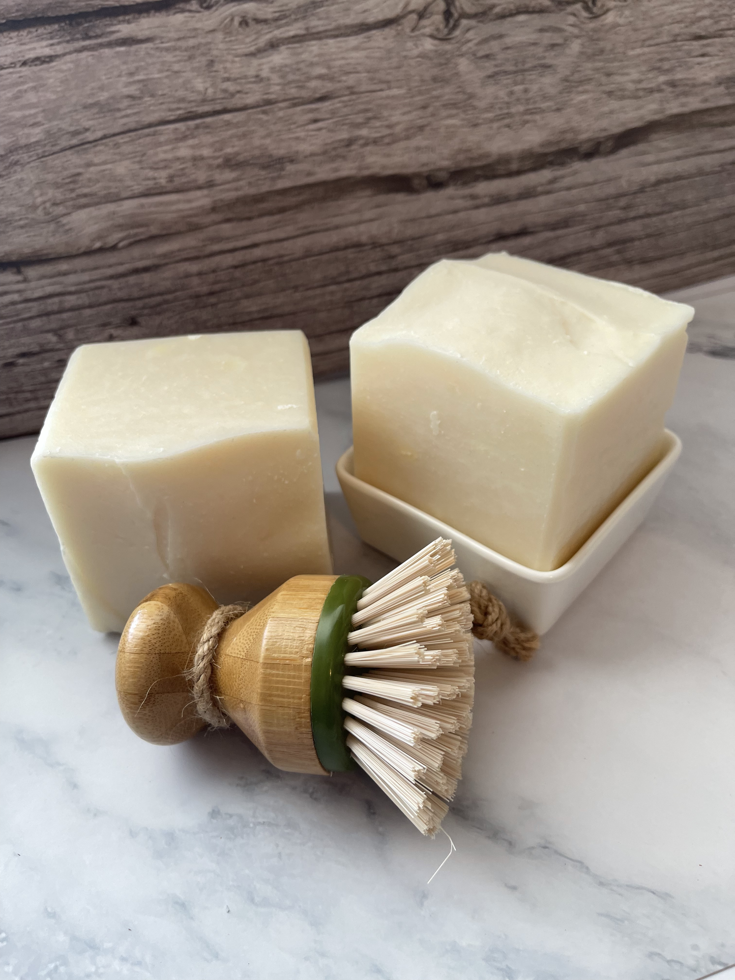 Two bars of soap and a wooden brush on a marble surface with a wooden background.