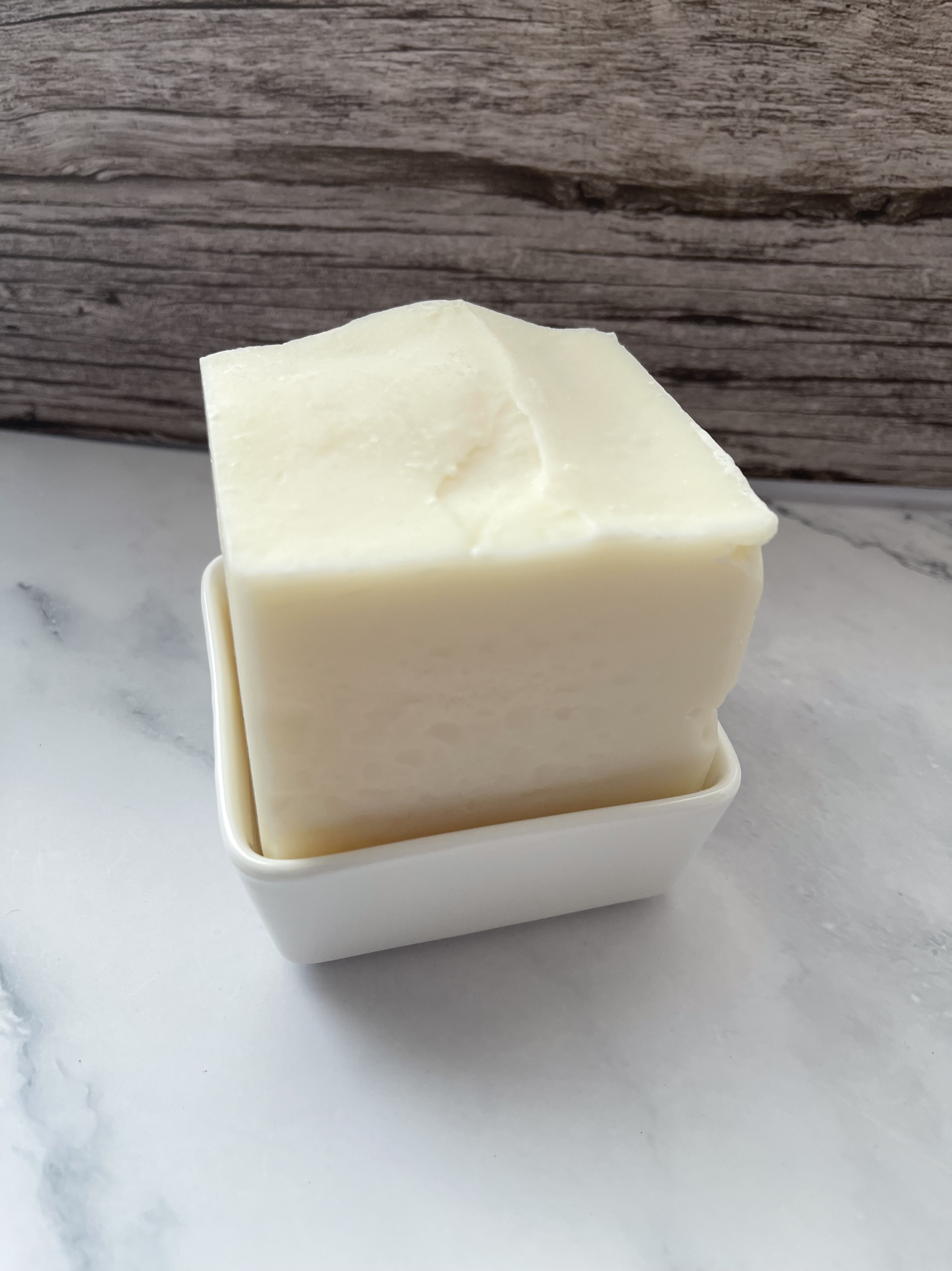 Two square bars of soap stacked on a white dish with a wooden background
