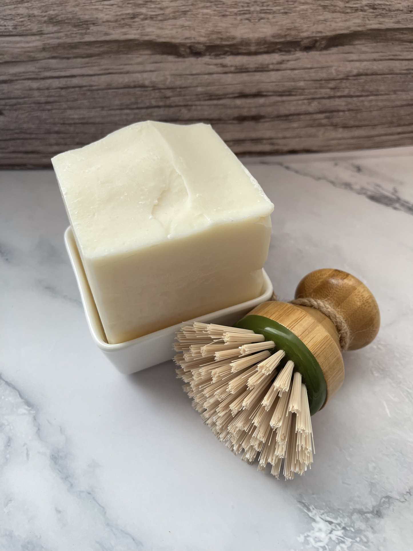 Bar of soap in a dish with a wooden-handled brush on a marble surface