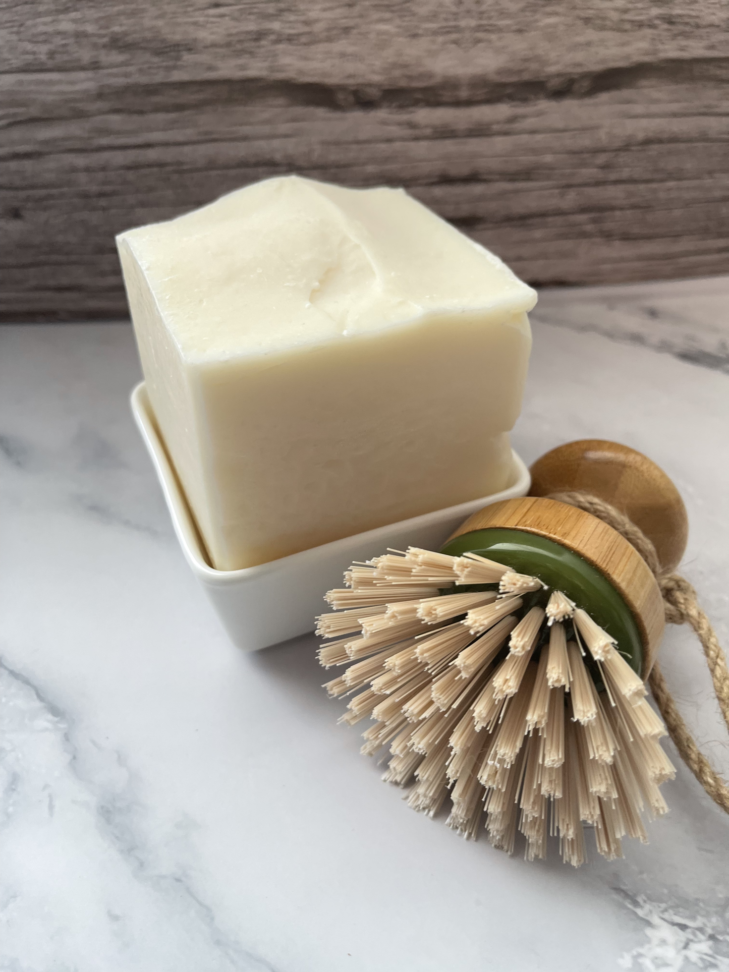 Bar of soap in a dish with a natural bristle brush on a marble surface
