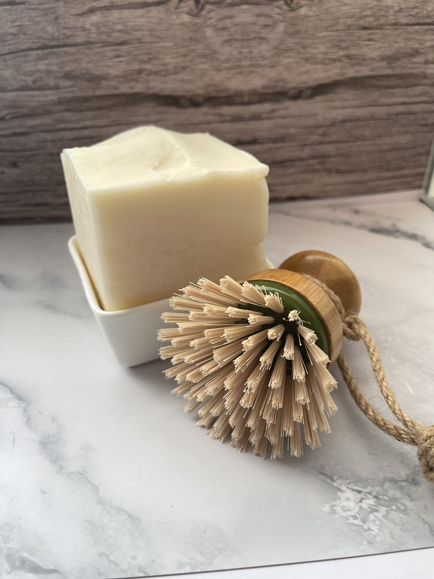 Bar of soap in a white dish with a natural bristle brush on a marble surface.