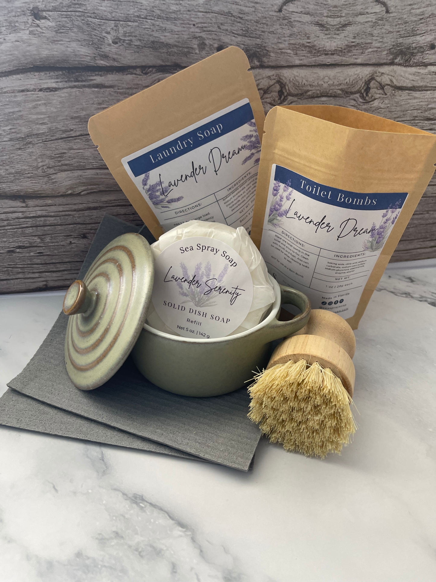 Set of bath products including a bar of soap, a scrub brush, and a container on a marble surface.