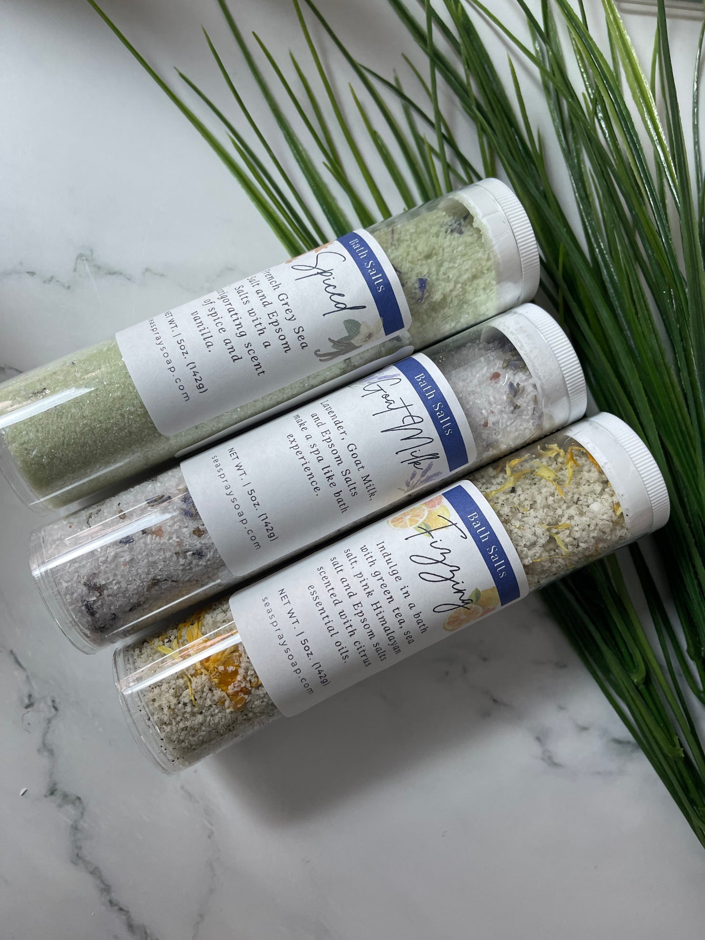 Three bath salt tubes with labels on a marble surface with green leaves.
