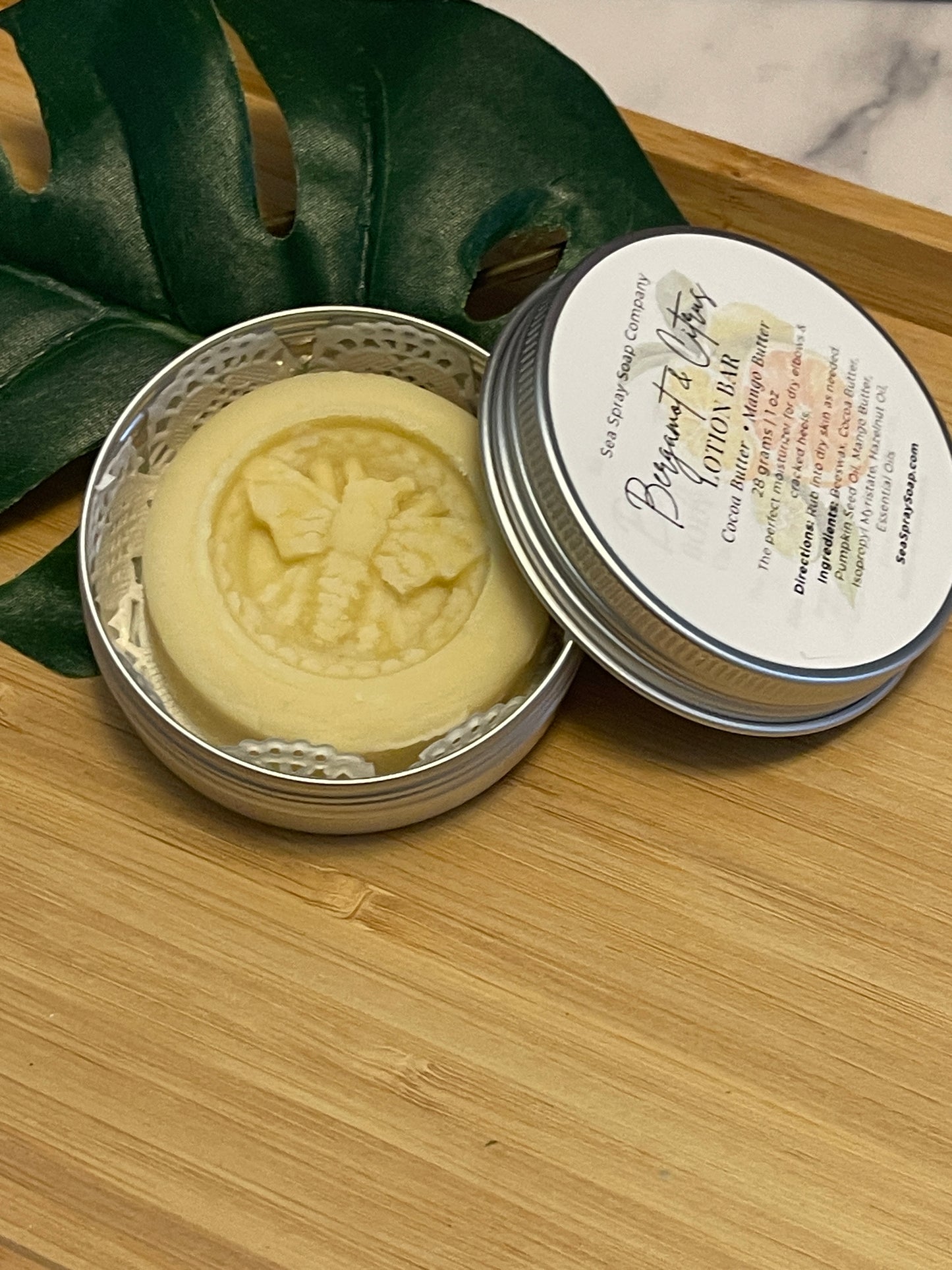 Bar of soap in a metal container on a wooden surface with a leafy green plant.