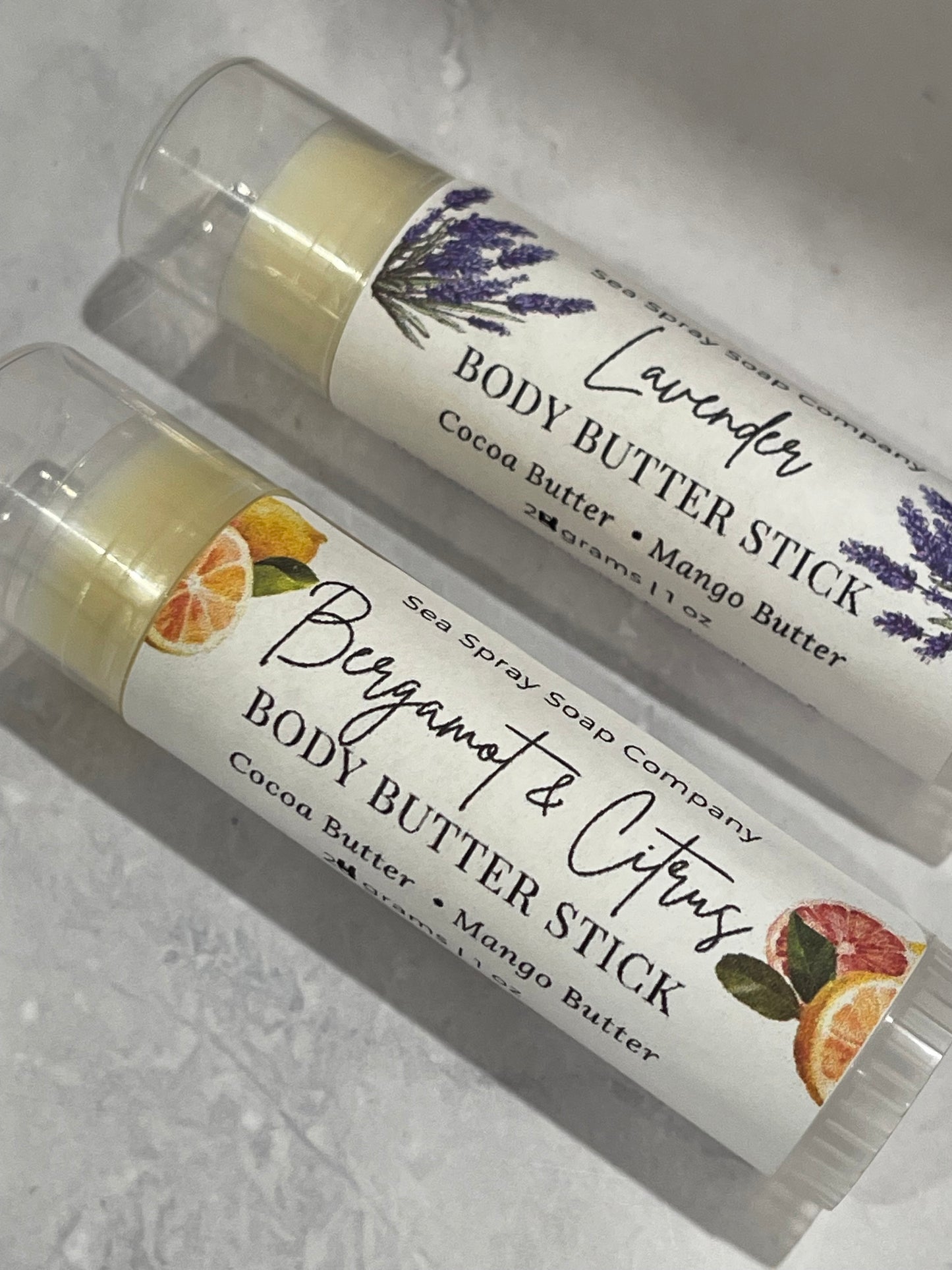 Two body butter sticks with labels on a gray surface