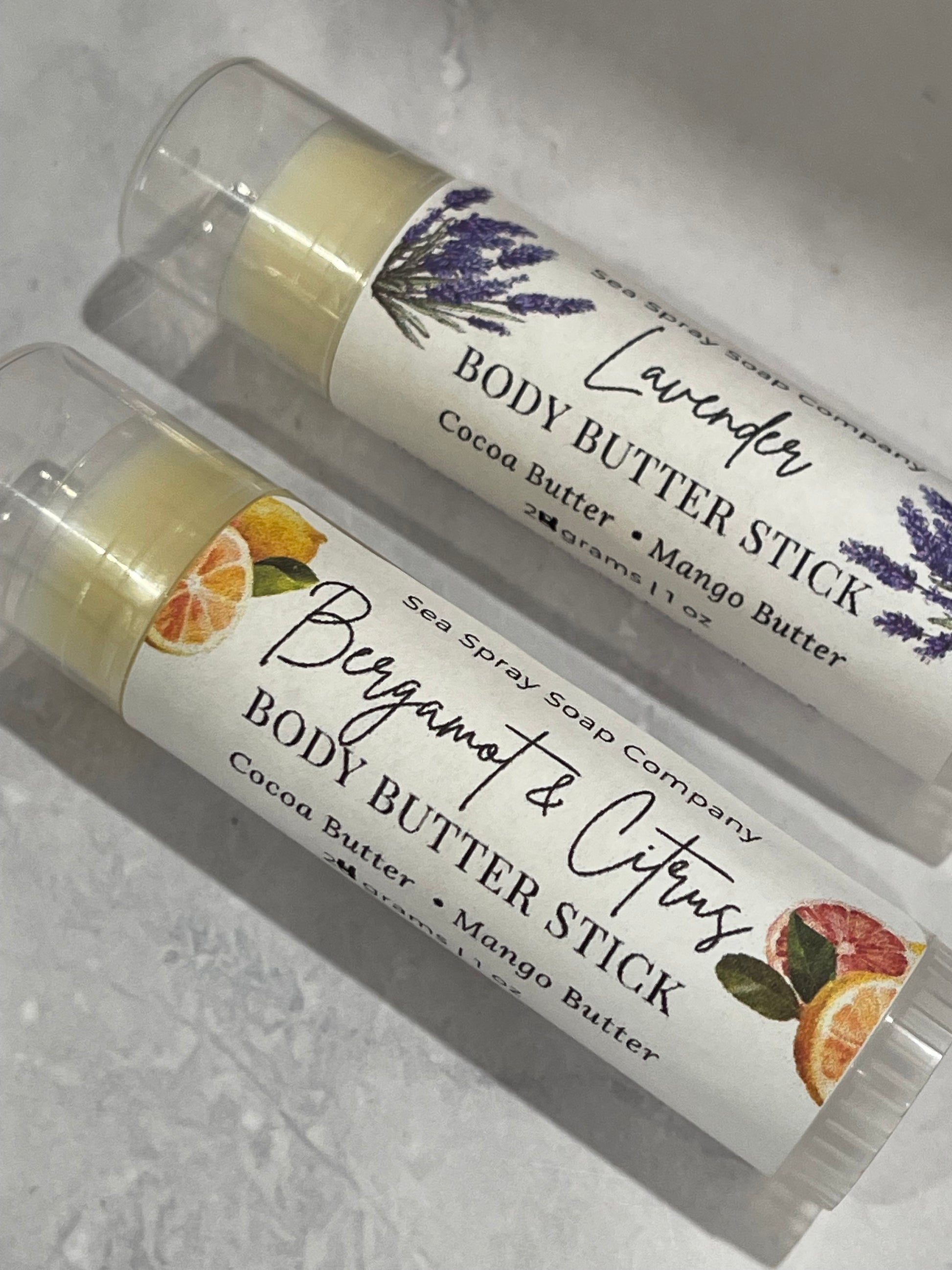 Two body butter sticks with labels on a gray surface