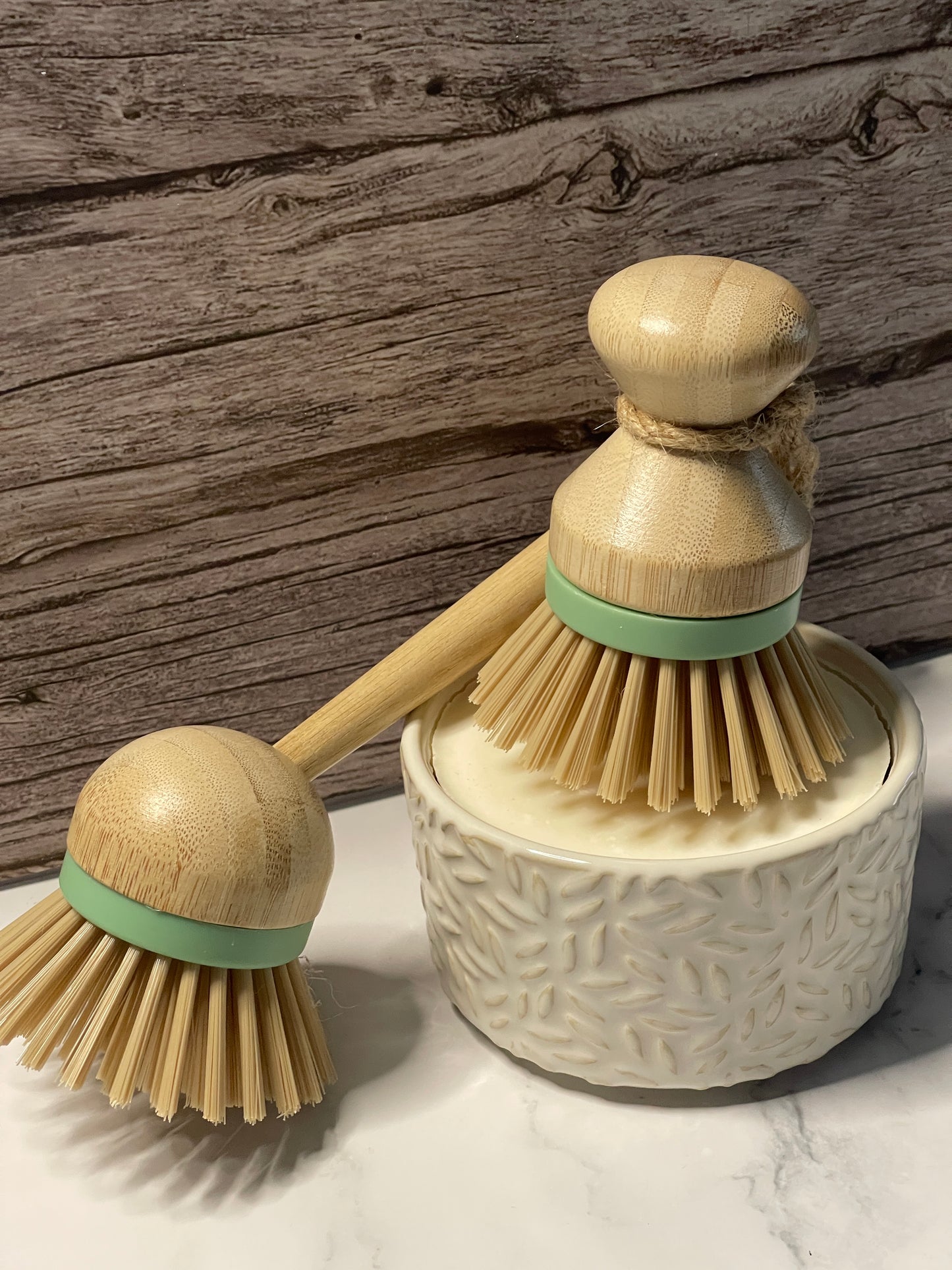 Set of two wooden dish brushes with green handles on a wooden surface.