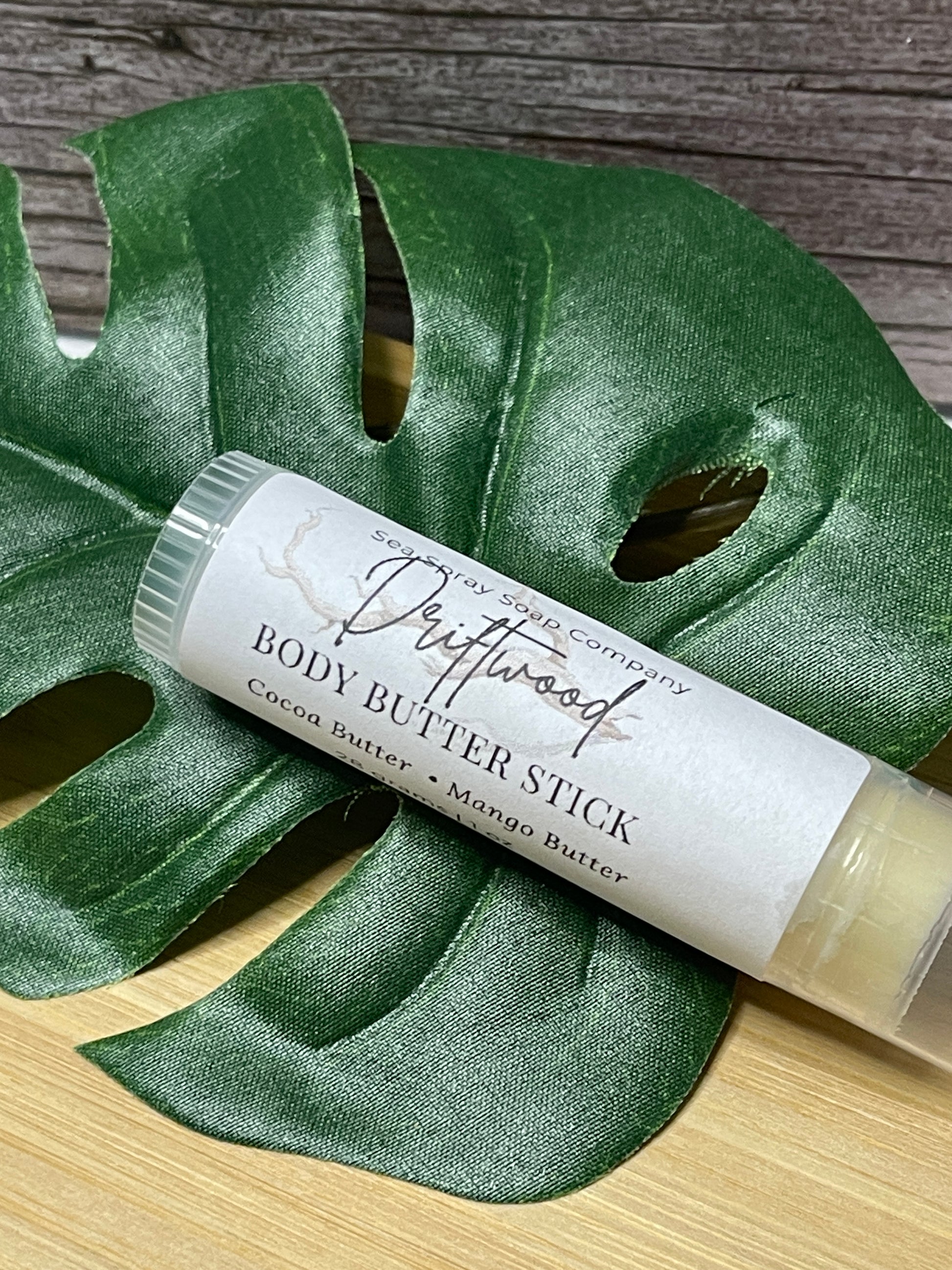 Body butter stick on a green leaf with a wooden background