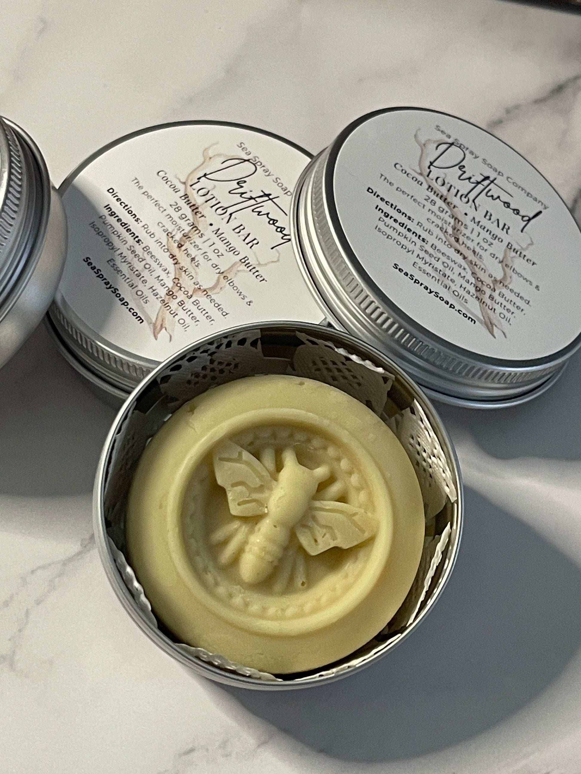 Butterfly-shaped soap in a metal tin with a decorative lid on a marble surface