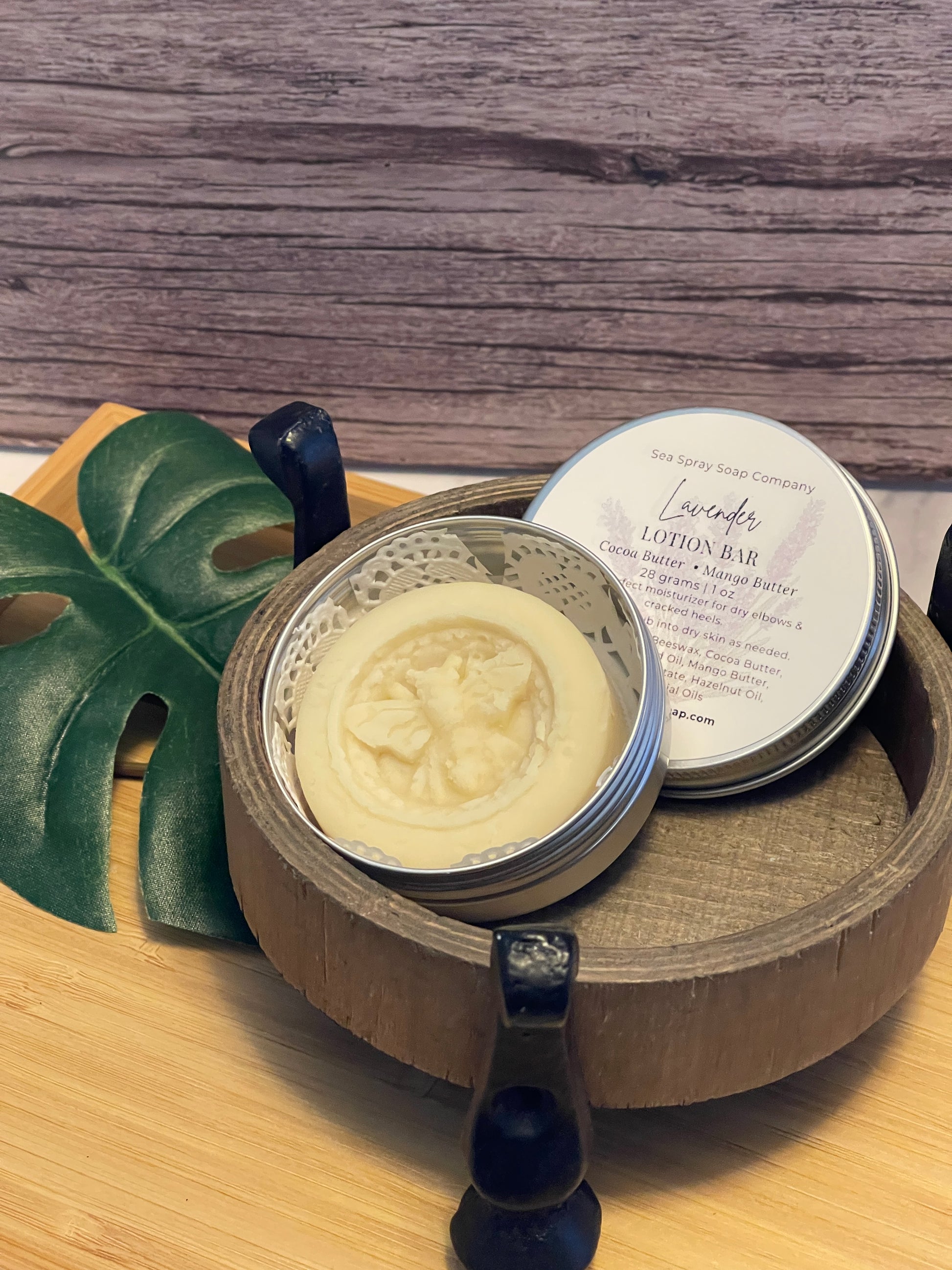 Bar of soap in a wooden dish on a wooden surface with a plant leaf in the foreground.