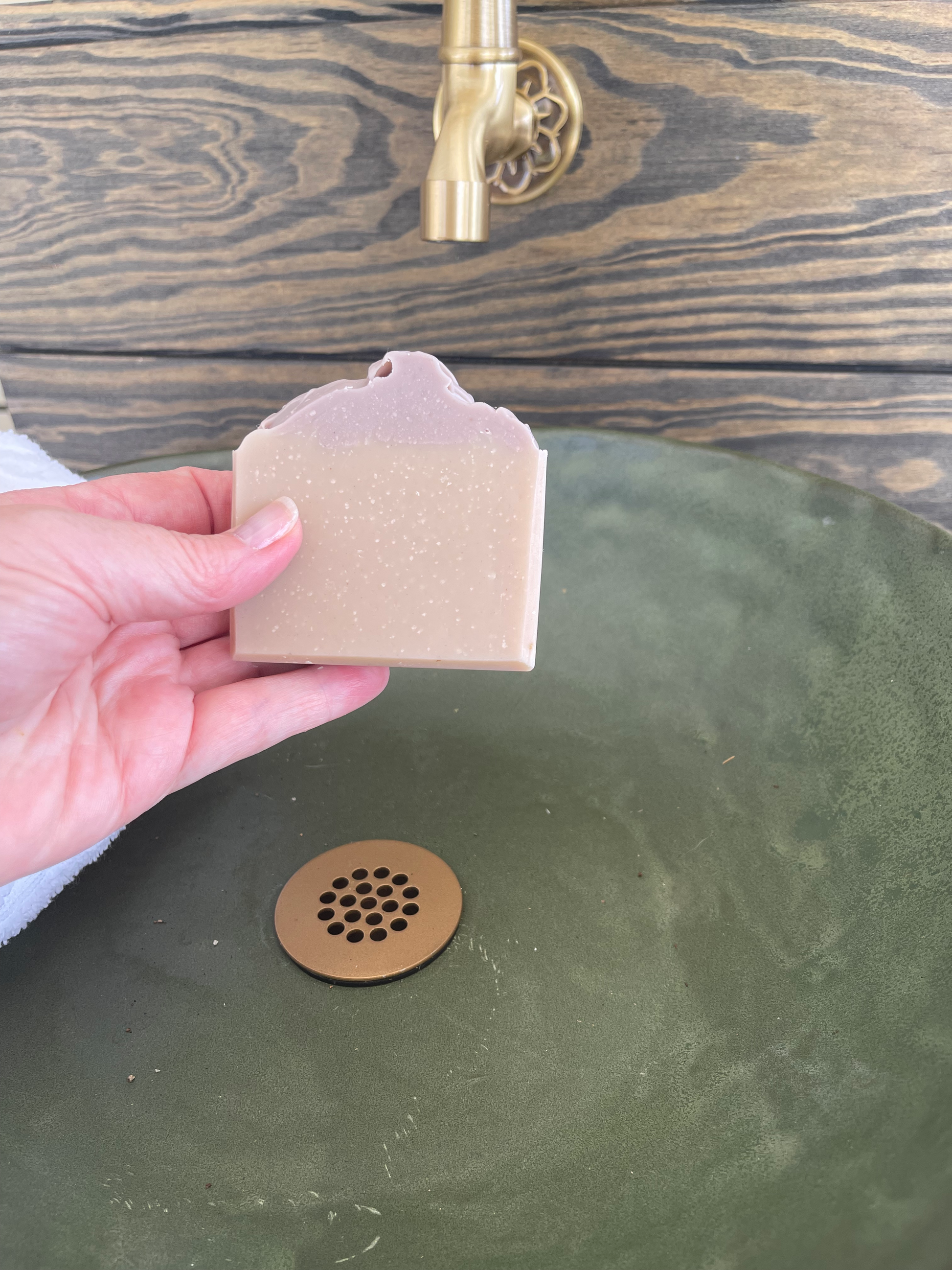 Hand holding a small brown box in front of a green sink with a brass drain cover.