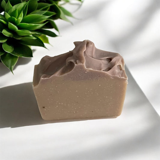 Bar of soap with a wavy top on a white surface with a green plant in the background