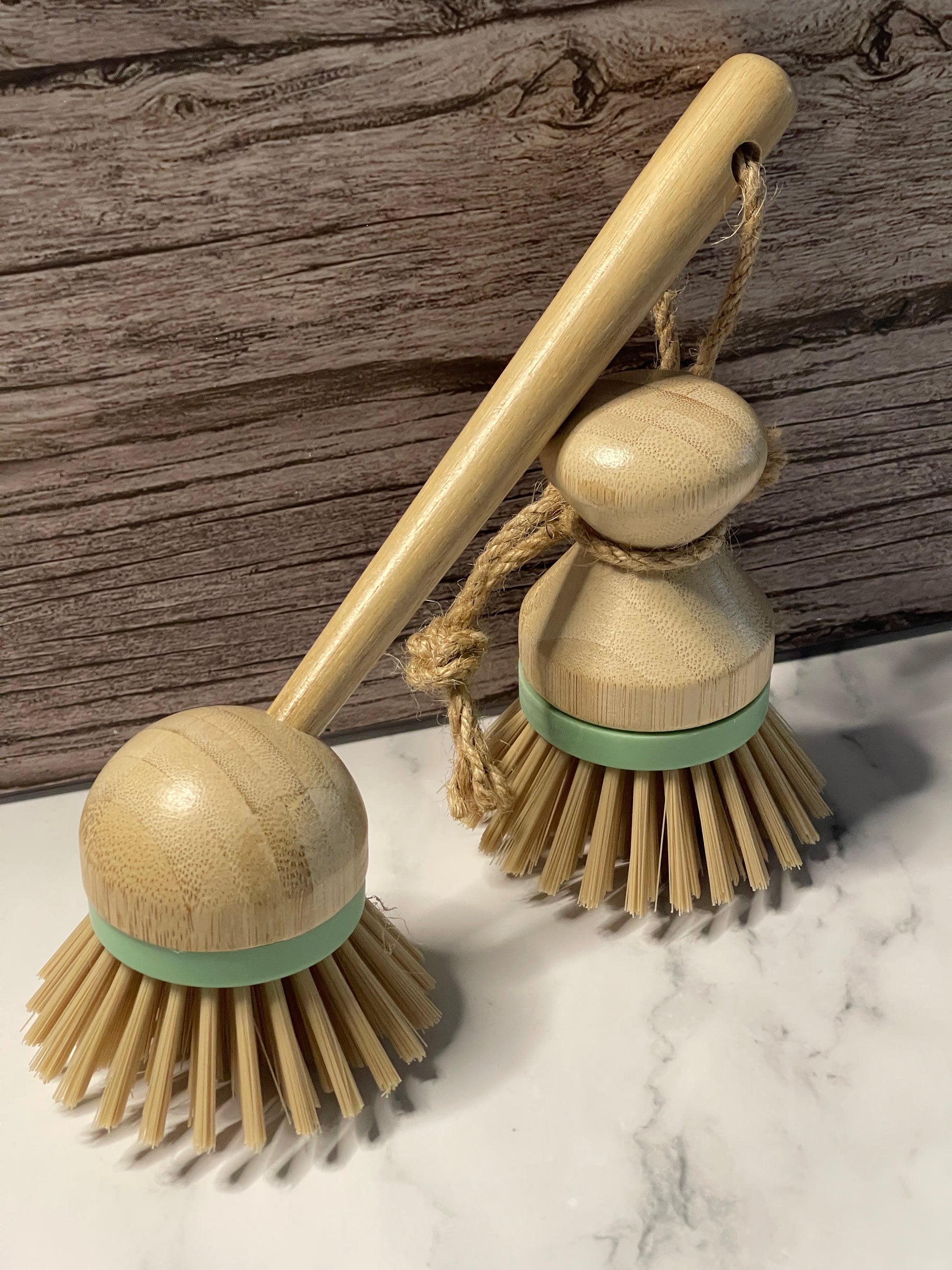 Two wooden dish brushes with green handles on a marble surface.