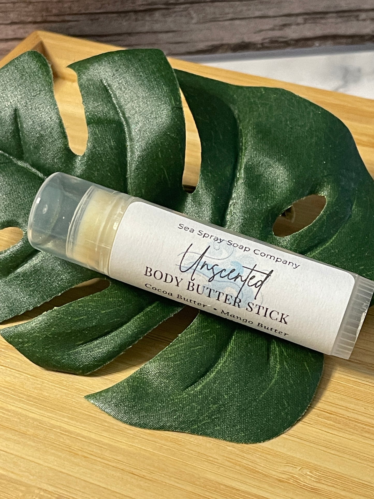 Body butter stick on a large green leaf with a wooden background