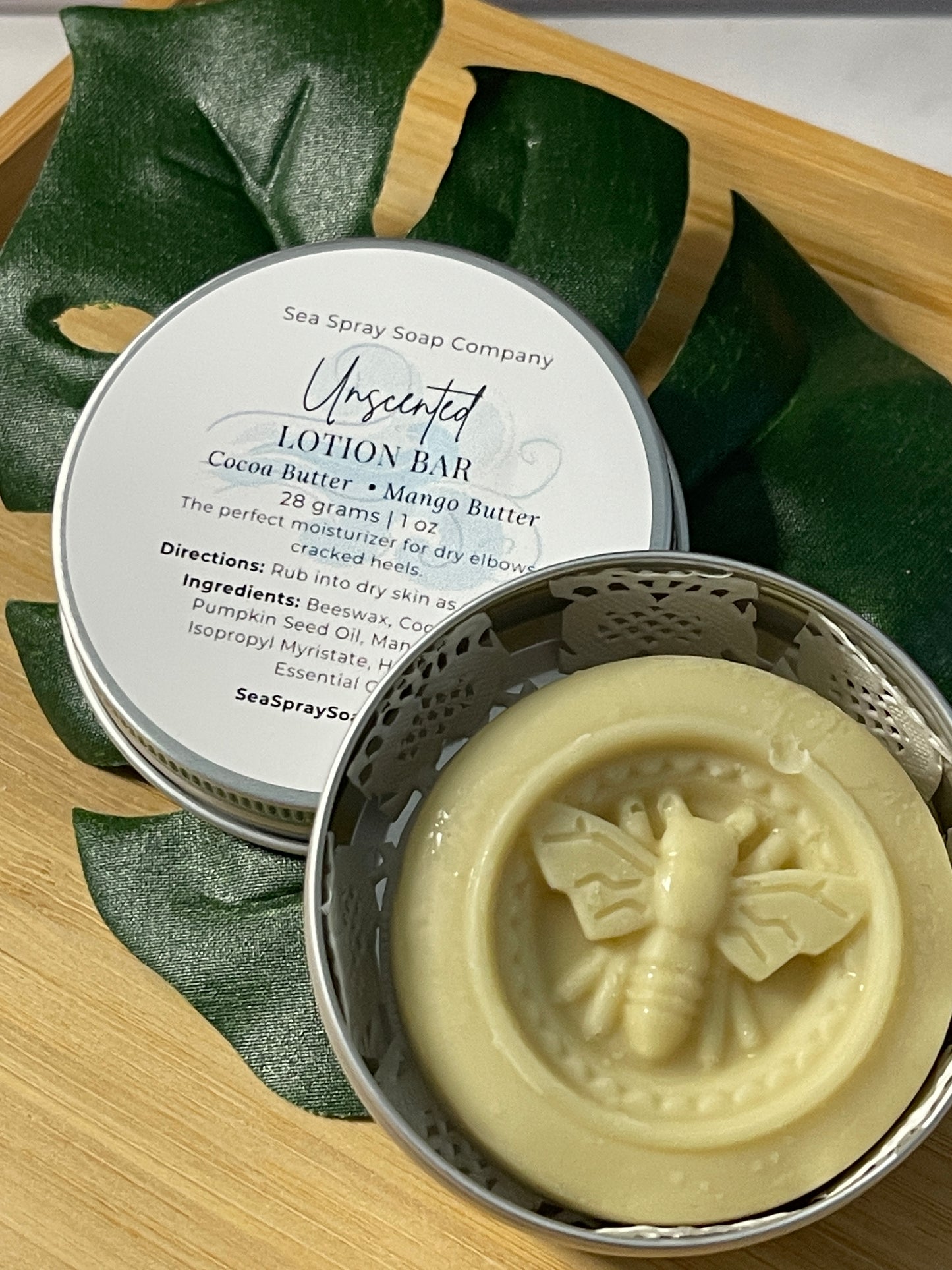 Unwrapped lotion bar with a decorative design on a wooden surface with green leaves.