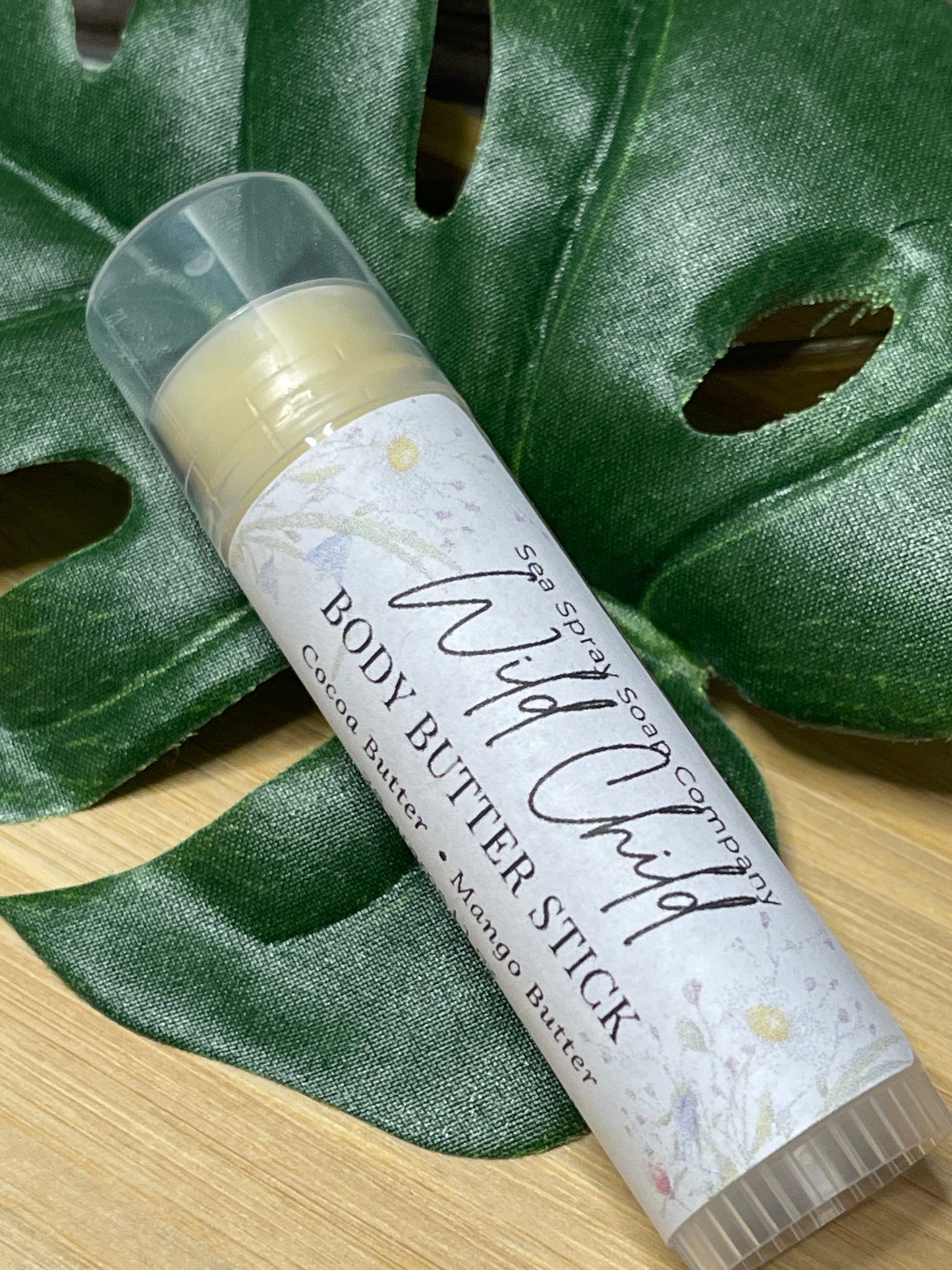 Body butter stick with 'Wild Child' label on a green leaf background