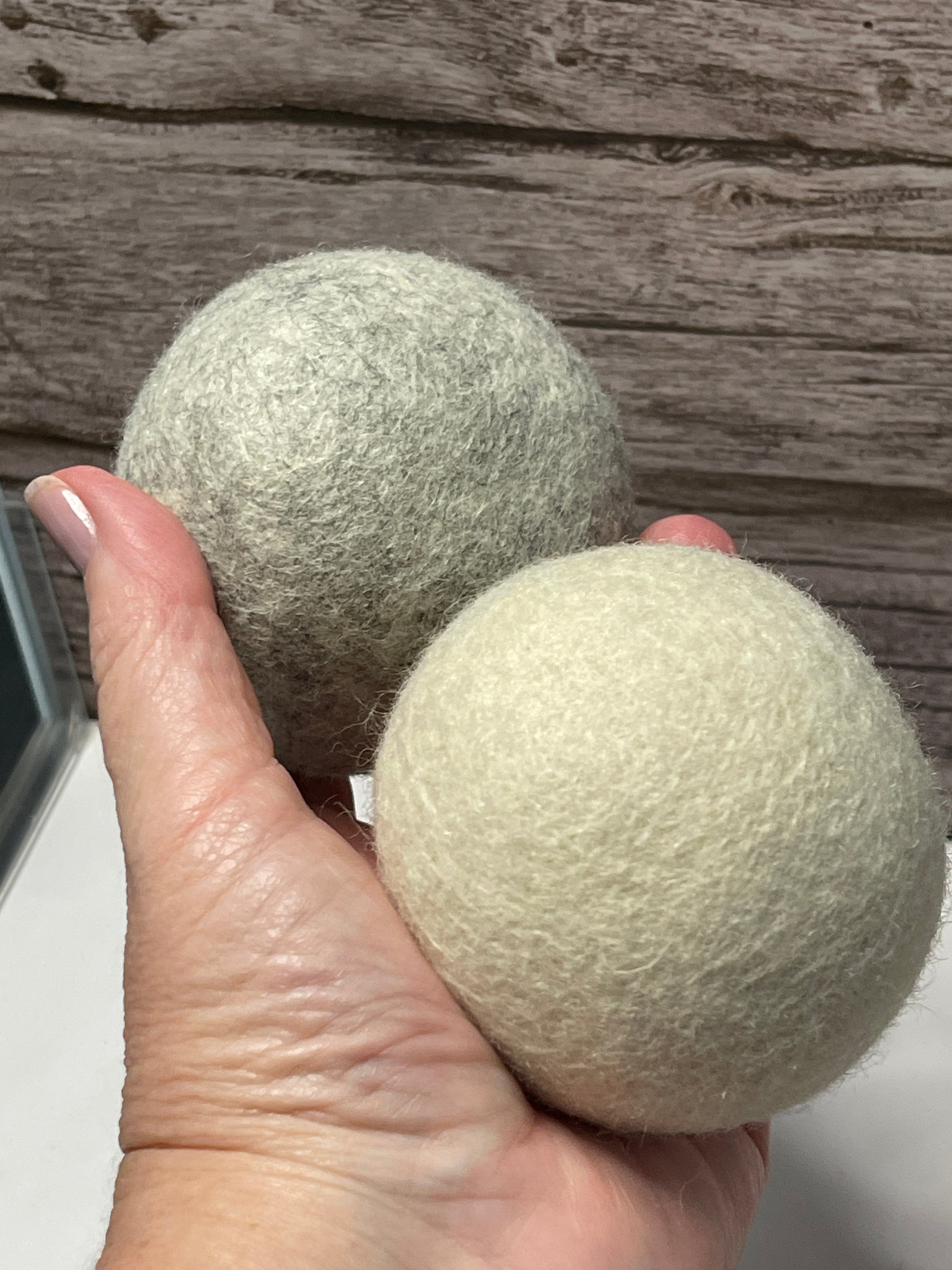 Two green wool dryer balls held by a hand against a wooden background