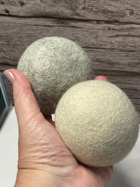 Two green wool dryer balls held by a hand against a wooden background