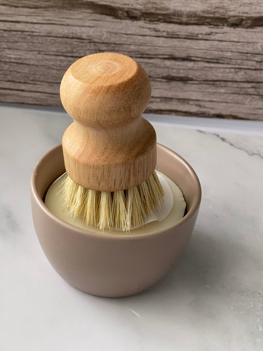 Shaving brush with wooden handle and natural bristles in a beige holder on a marble surface.