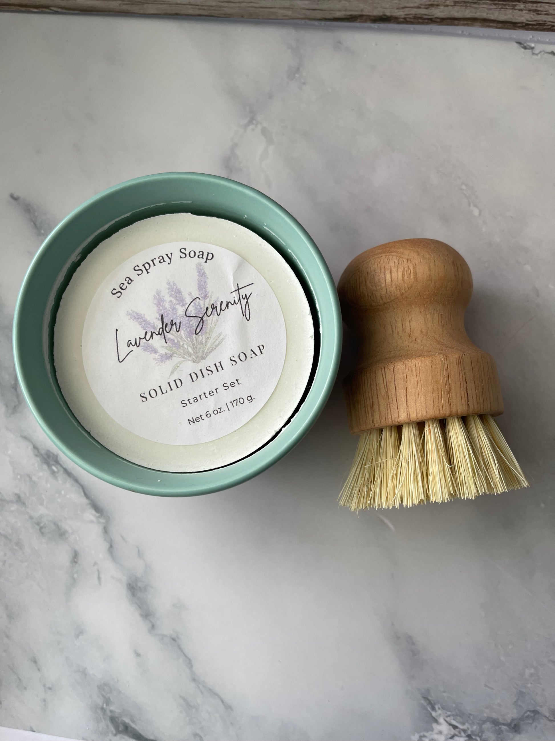 Bar of soap in a green container with a wooden brush on a marble surface