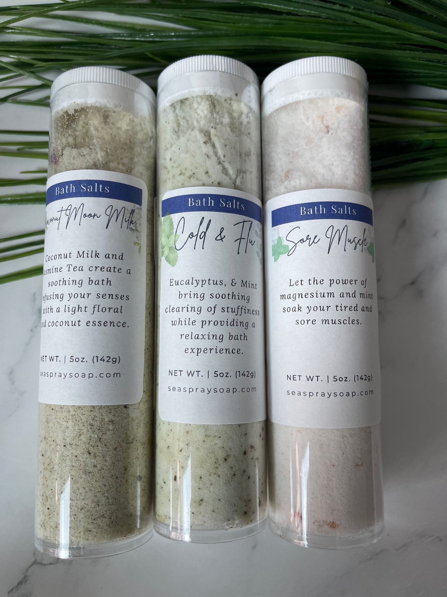 Three cylindrical containers of bath salts with labels on a marble surface.