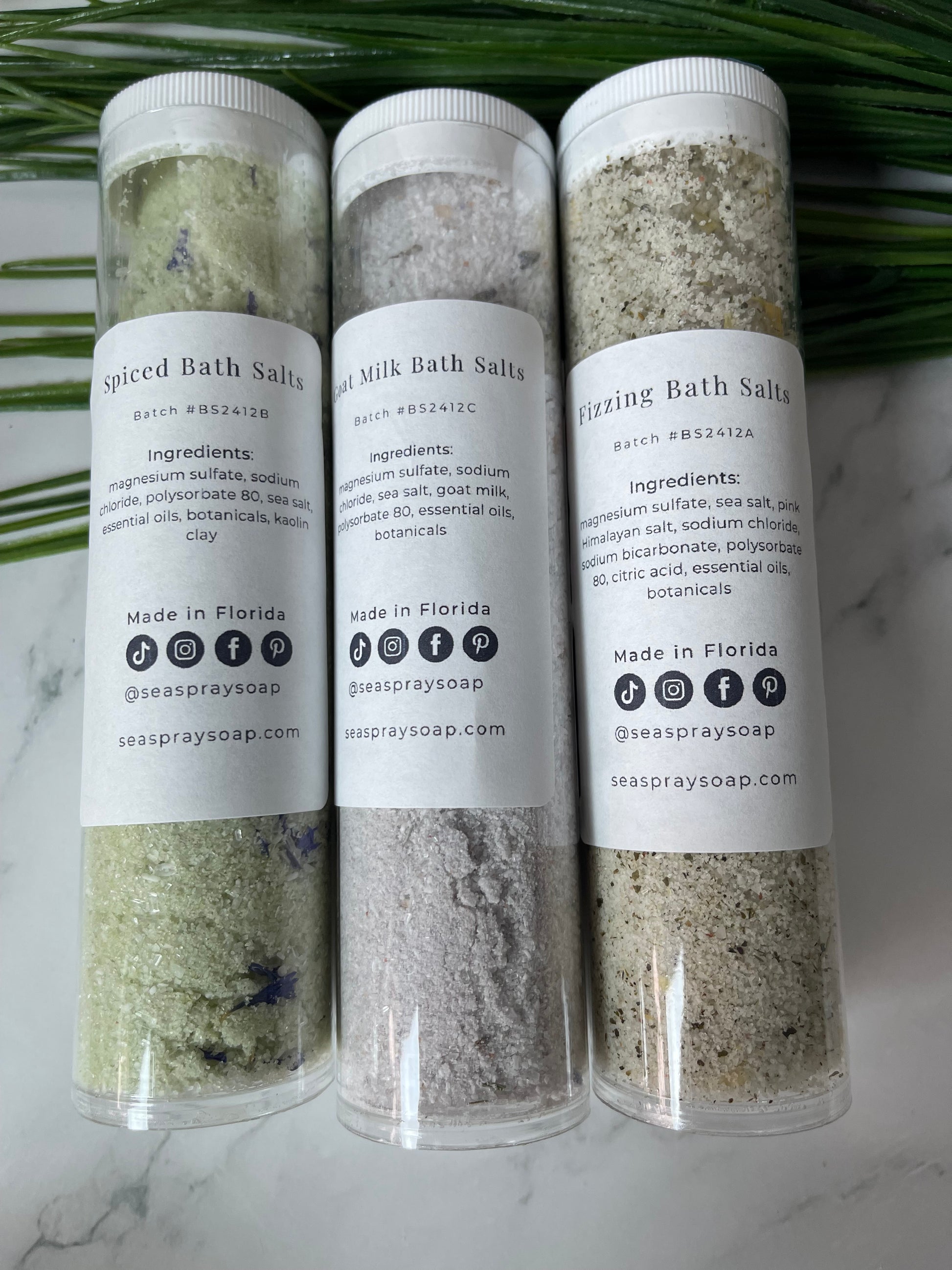Three tubes of milk bath salts on a marble surface with a green leaf.