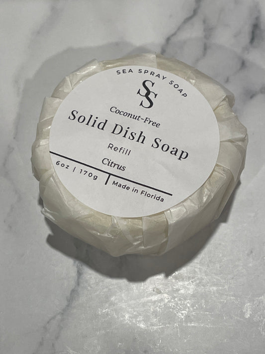 A wrapped round of Sea Spray Soap Solid Dish Soap refill, labeled Citrus, resting on a white marble surface.