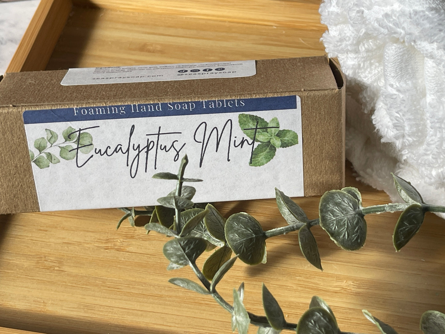 Box of Eucalyptus Mint foaming hand soap tablets on a wooden surface with eucalyptus leaves.