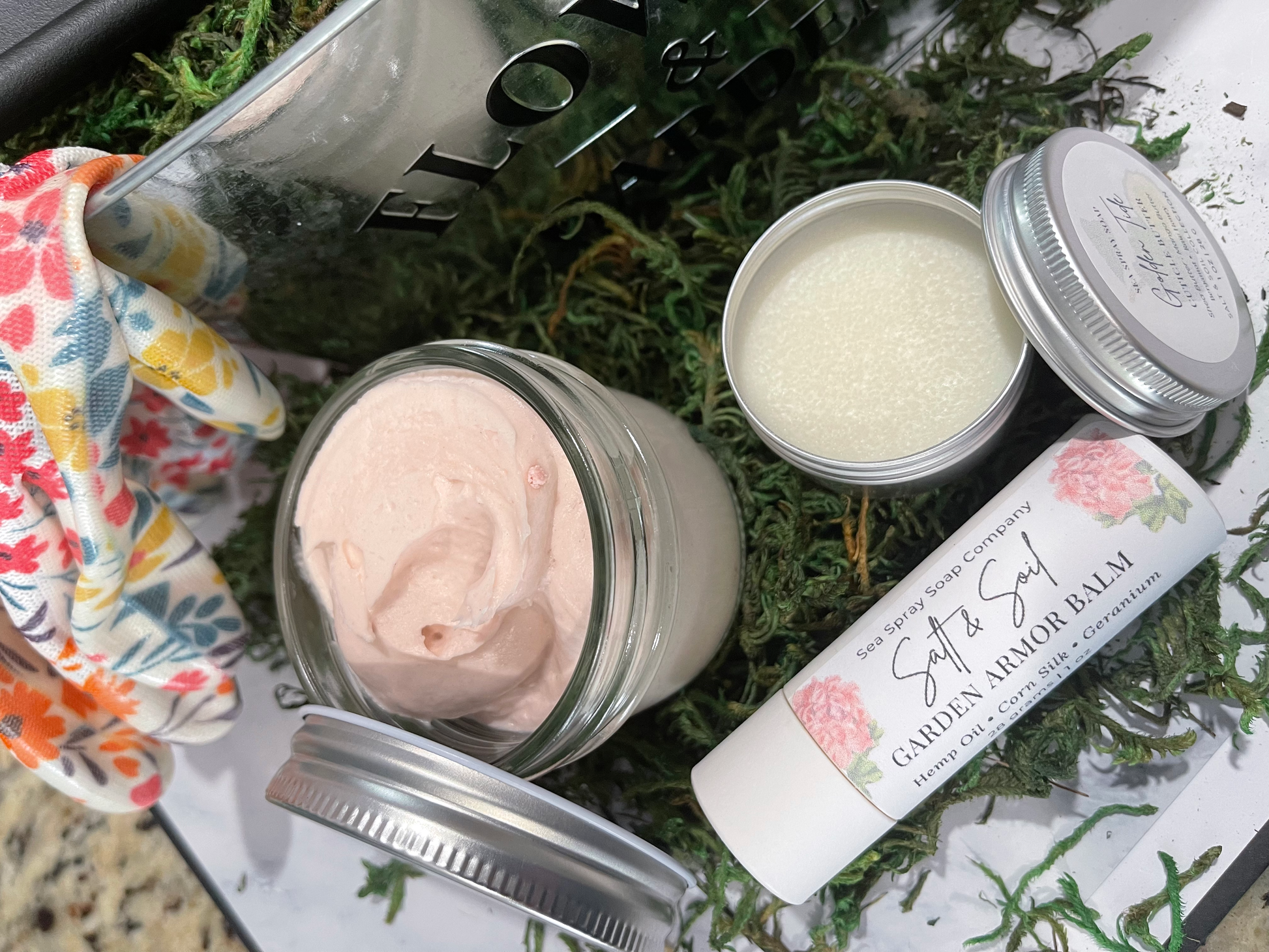 Cosmetic products including a jar of pink cream, a tube of balm, and a bottle of lotion on a green grass background.