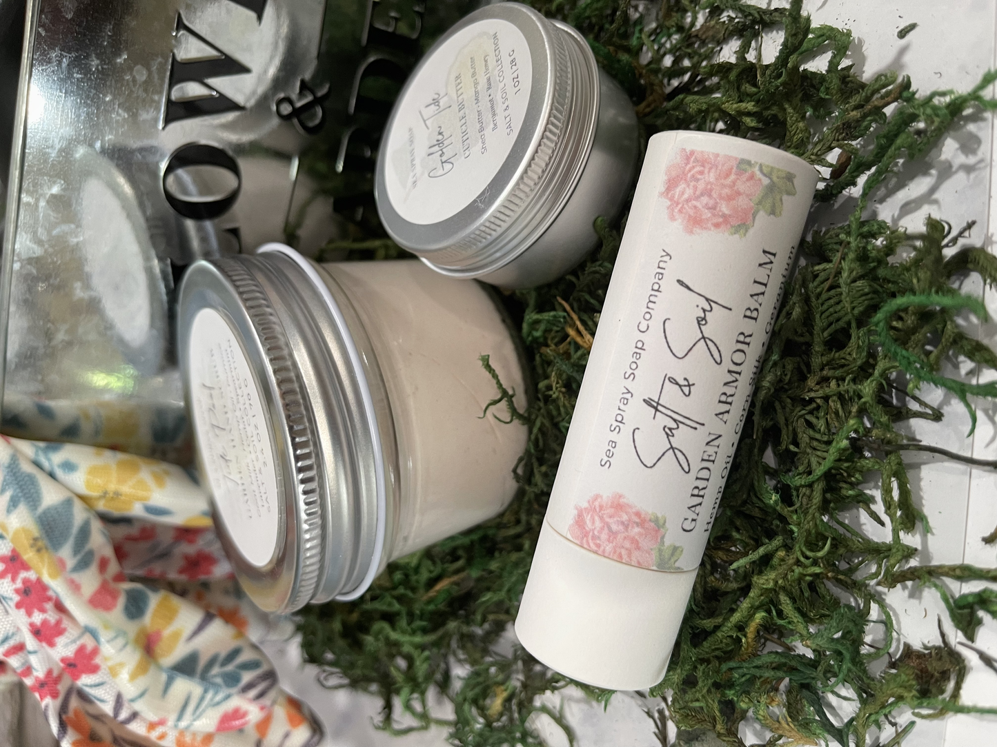 Balm jars and a stick of balm on a textured surface with greenery