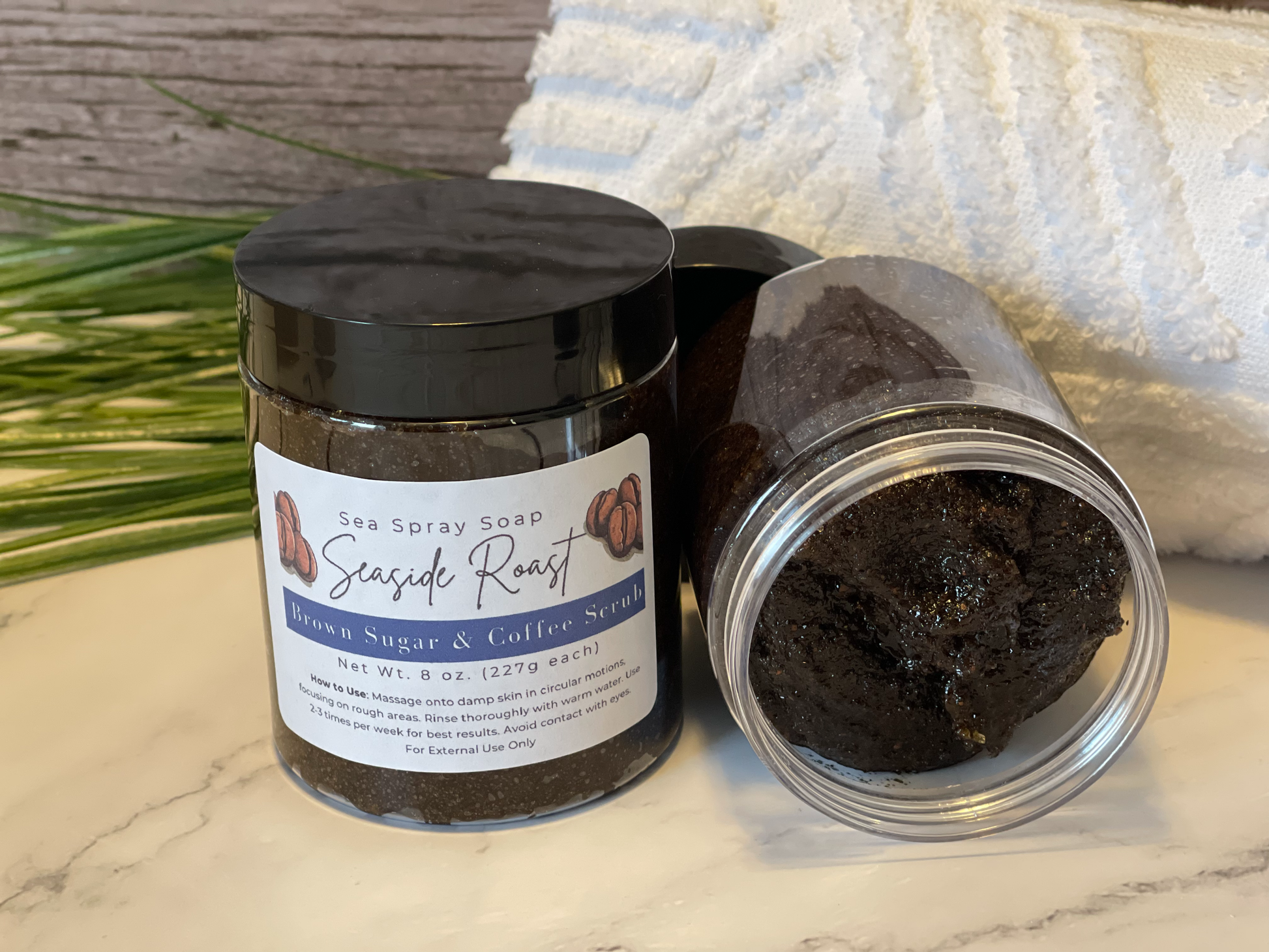Brown sugar and coffee scrub in a jar with a black lid on a marble surface.