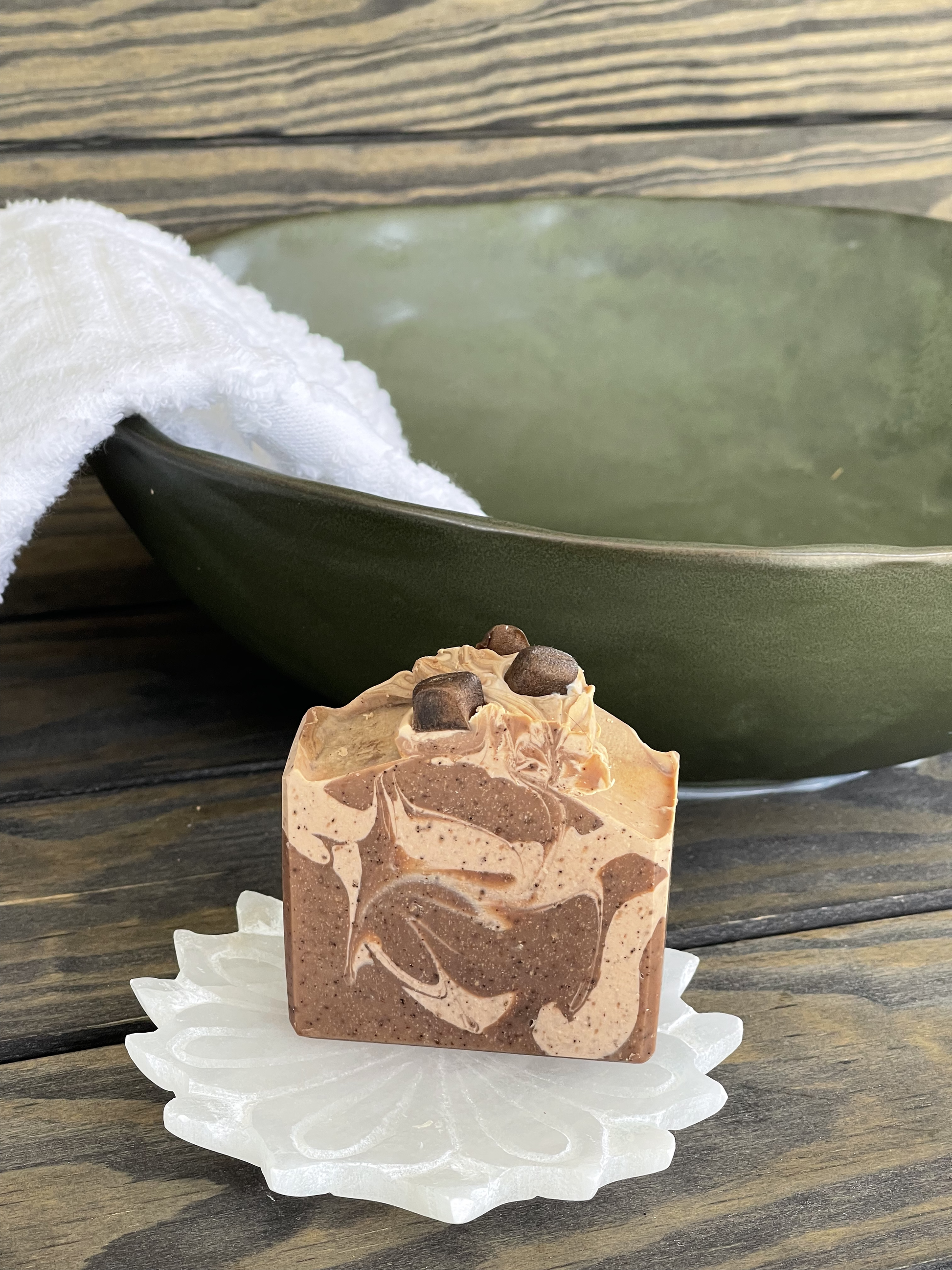 Bar of soap with chocolate chips on a decorative soap dish in front of a green bowl.
