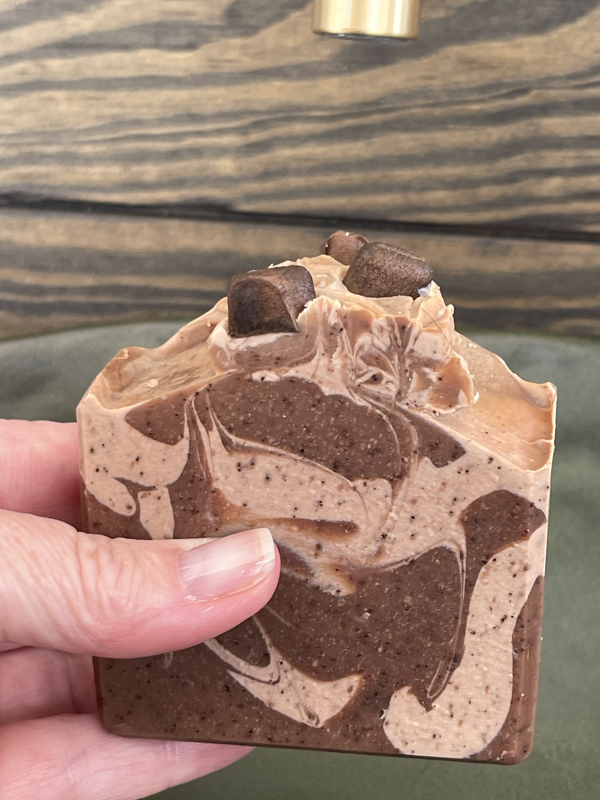 Hand holding a marbled brown and beige soap bar against a wooden background