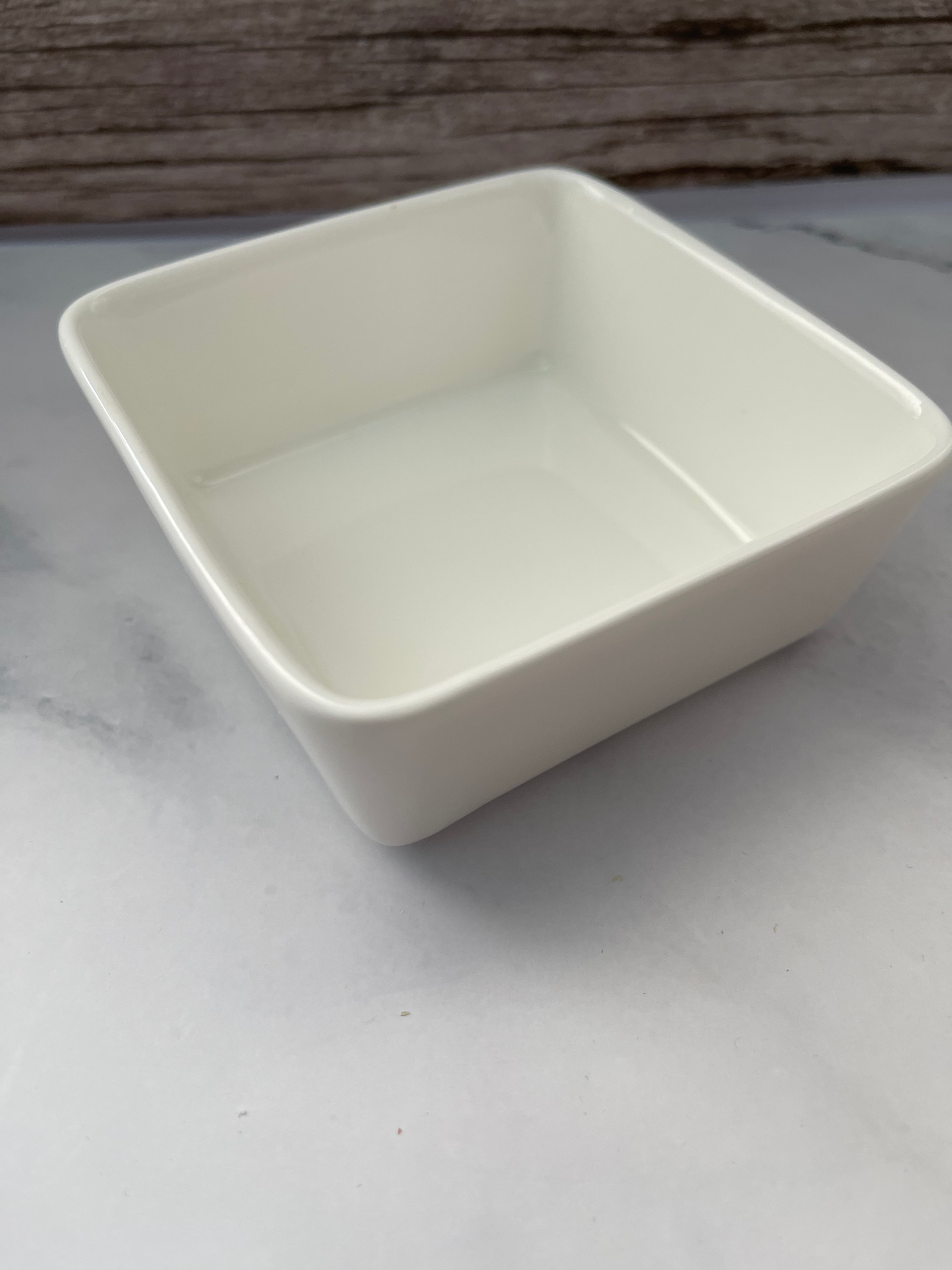 Two large white solid dish soap blocks next to a bamboo dish brush on a marble surface with a wooden wall in the background.