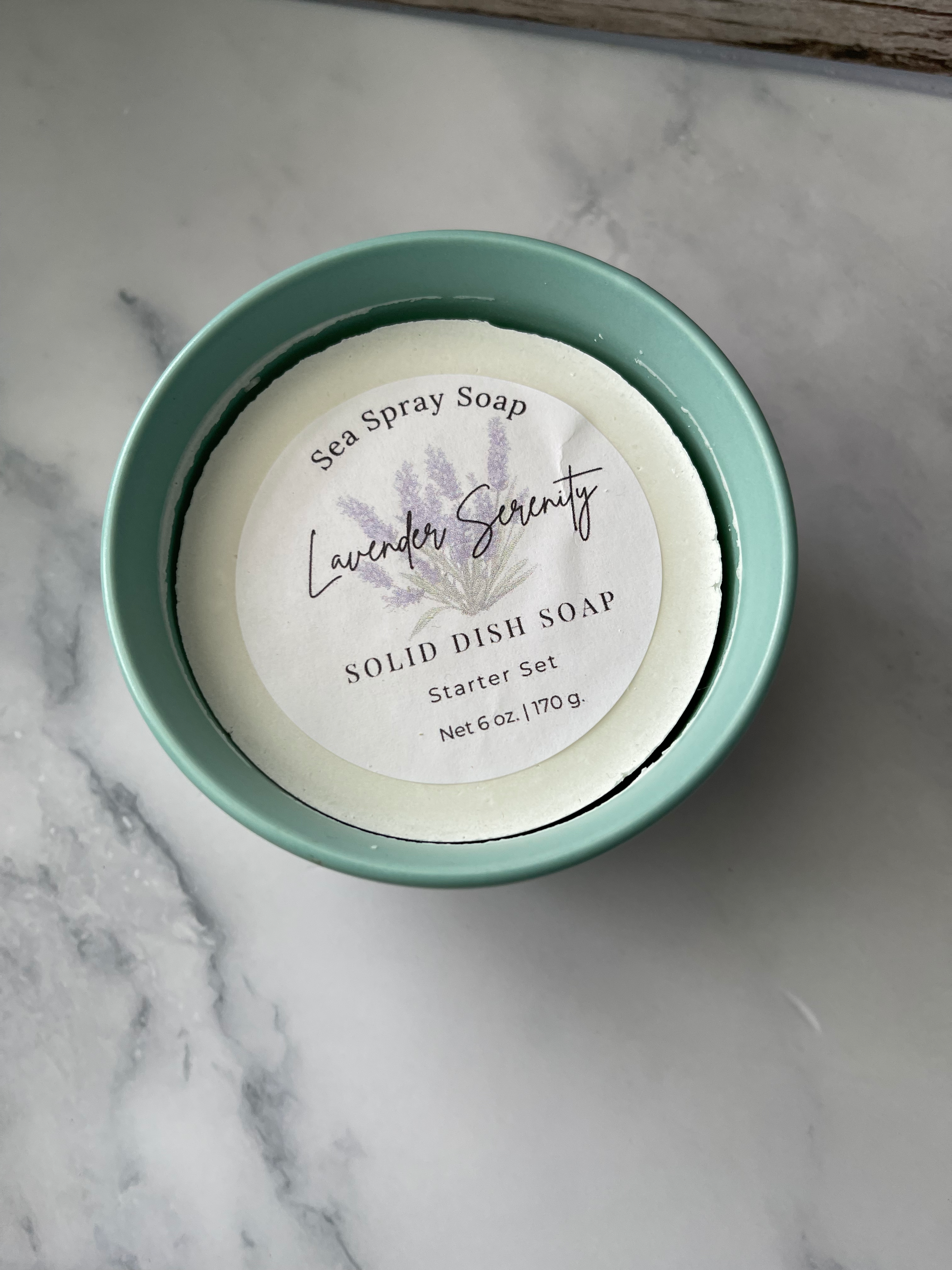 Solid dish soap in a green container on a marble surface