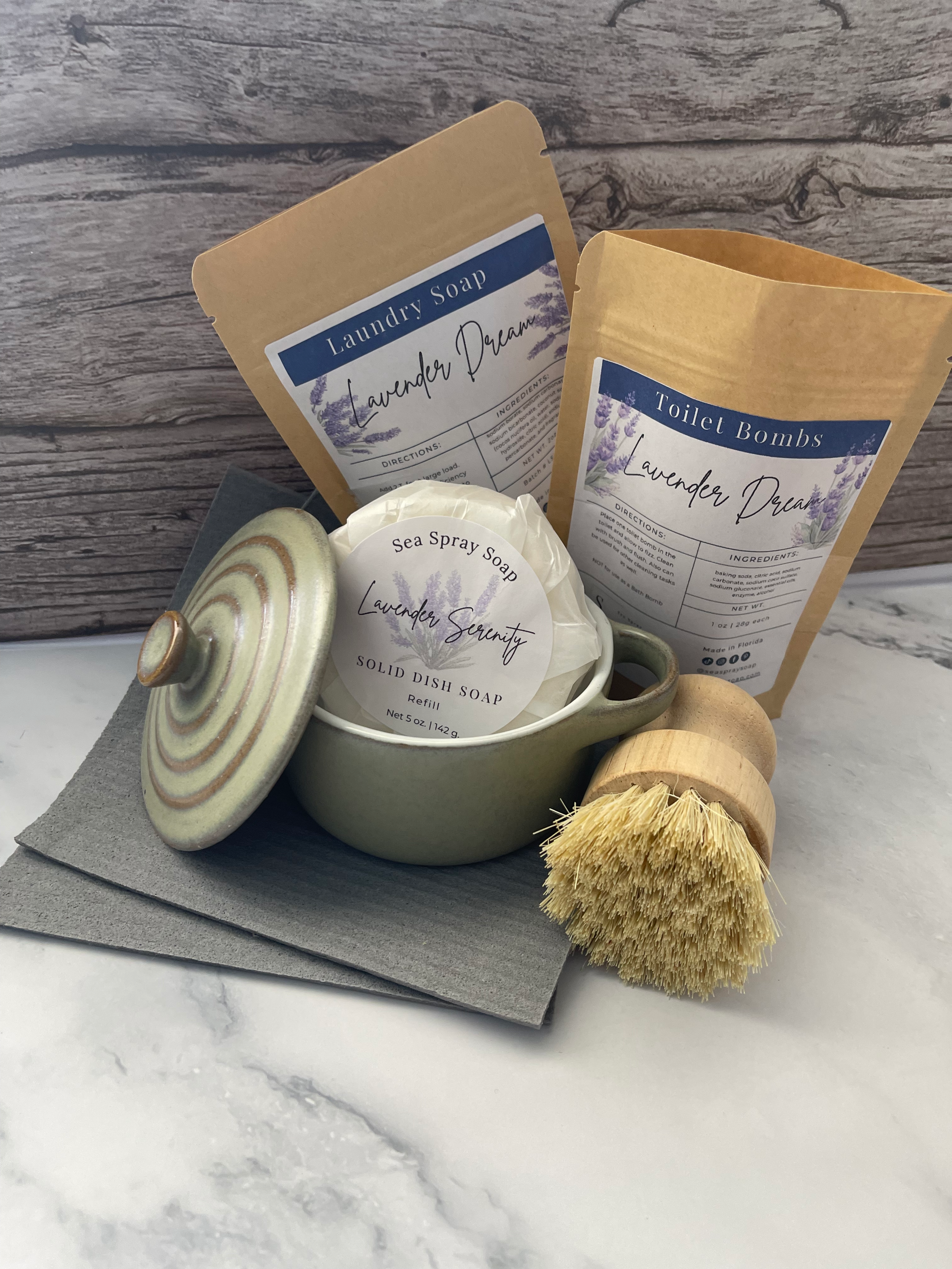 Set of bath products including a bar of soap, a scrub brush, and a container on a marble surface.