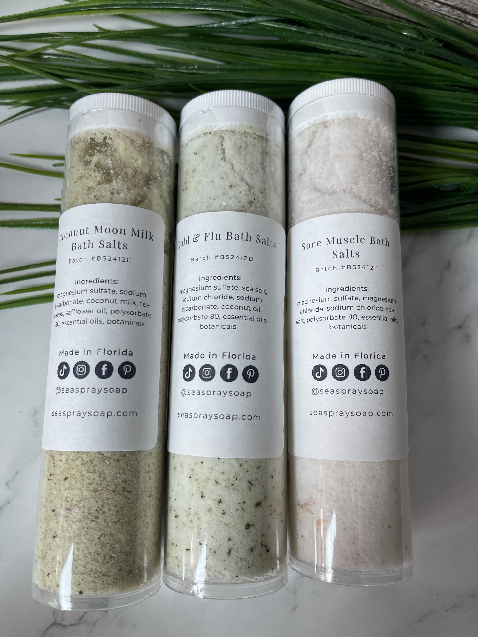 Three cylindrical containers of bath salts with labels on a marble surface.