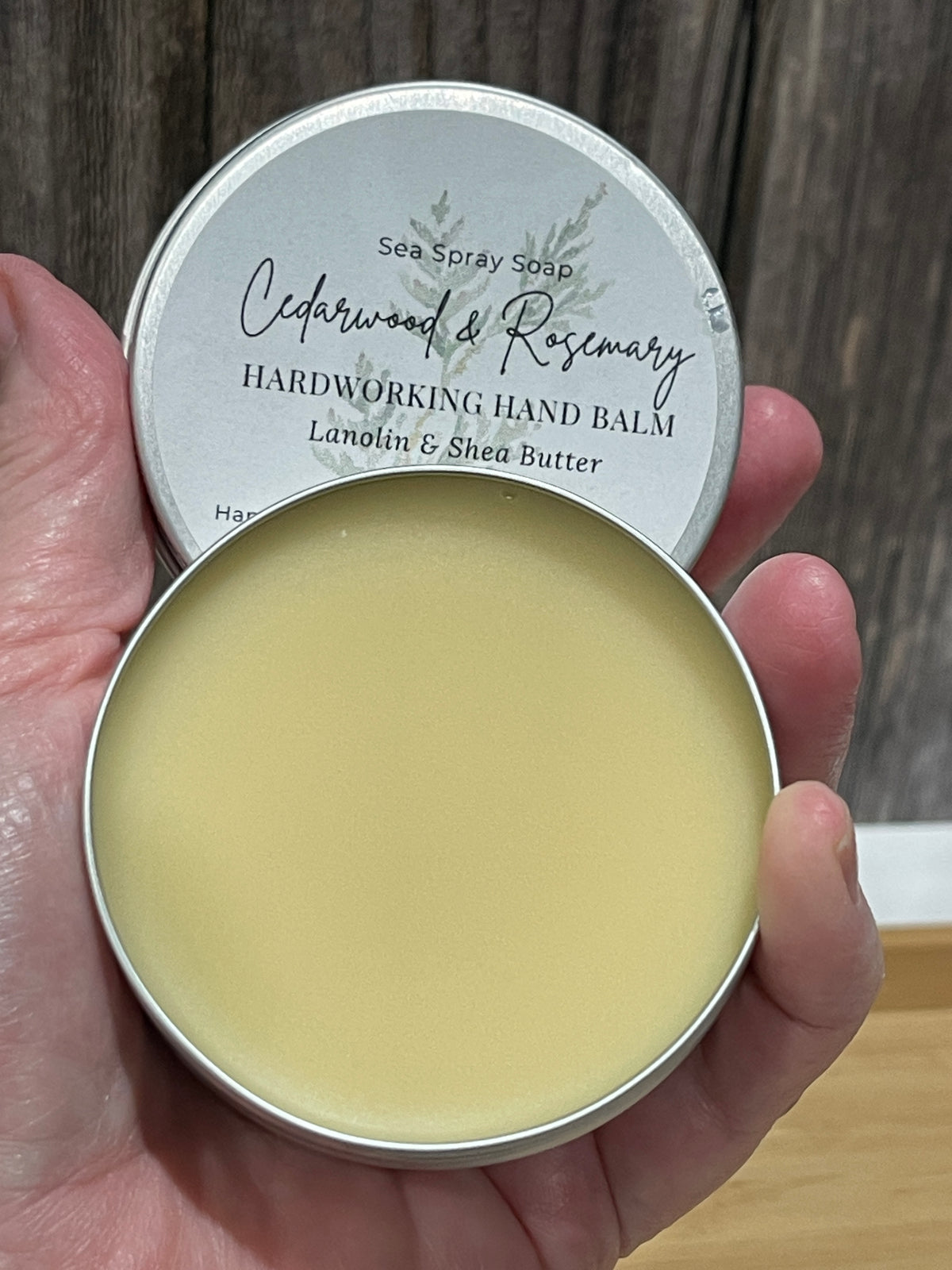 Hand holding the hardworking hand balm scented with essential oils in a 2 oz tin.