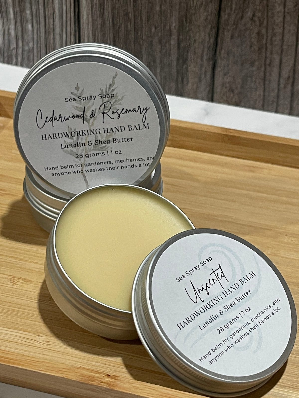 Tins of hardworking hand balm in unscented and cedarwood & rosemary on a bamboo tray.