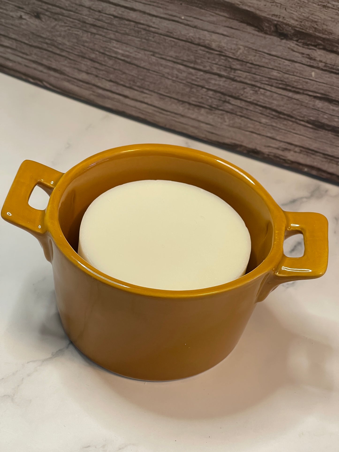 Yellow ceramic dish with a white bar of soap on a marble surface