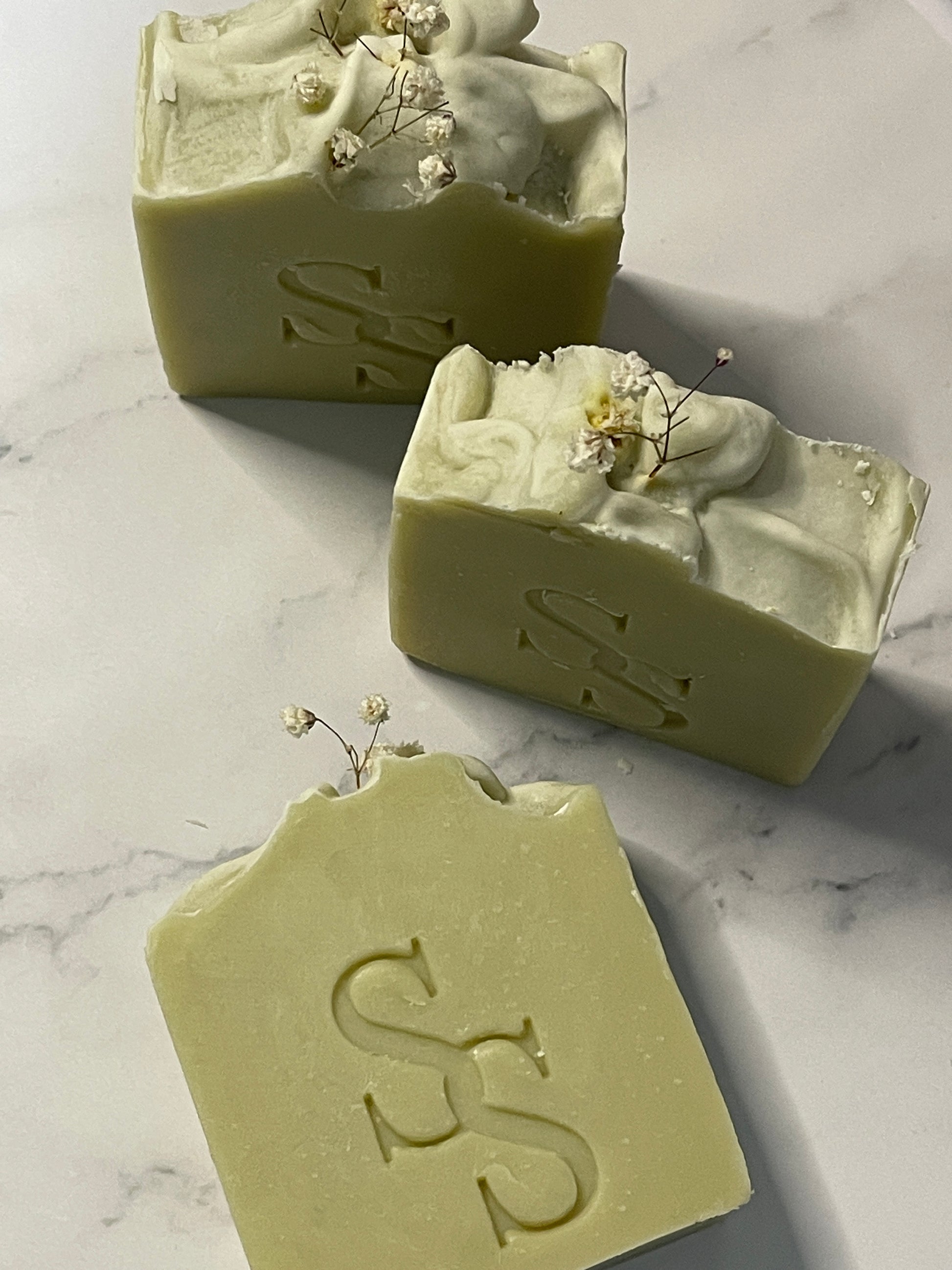Three green soap bars with a logo on a marble surface