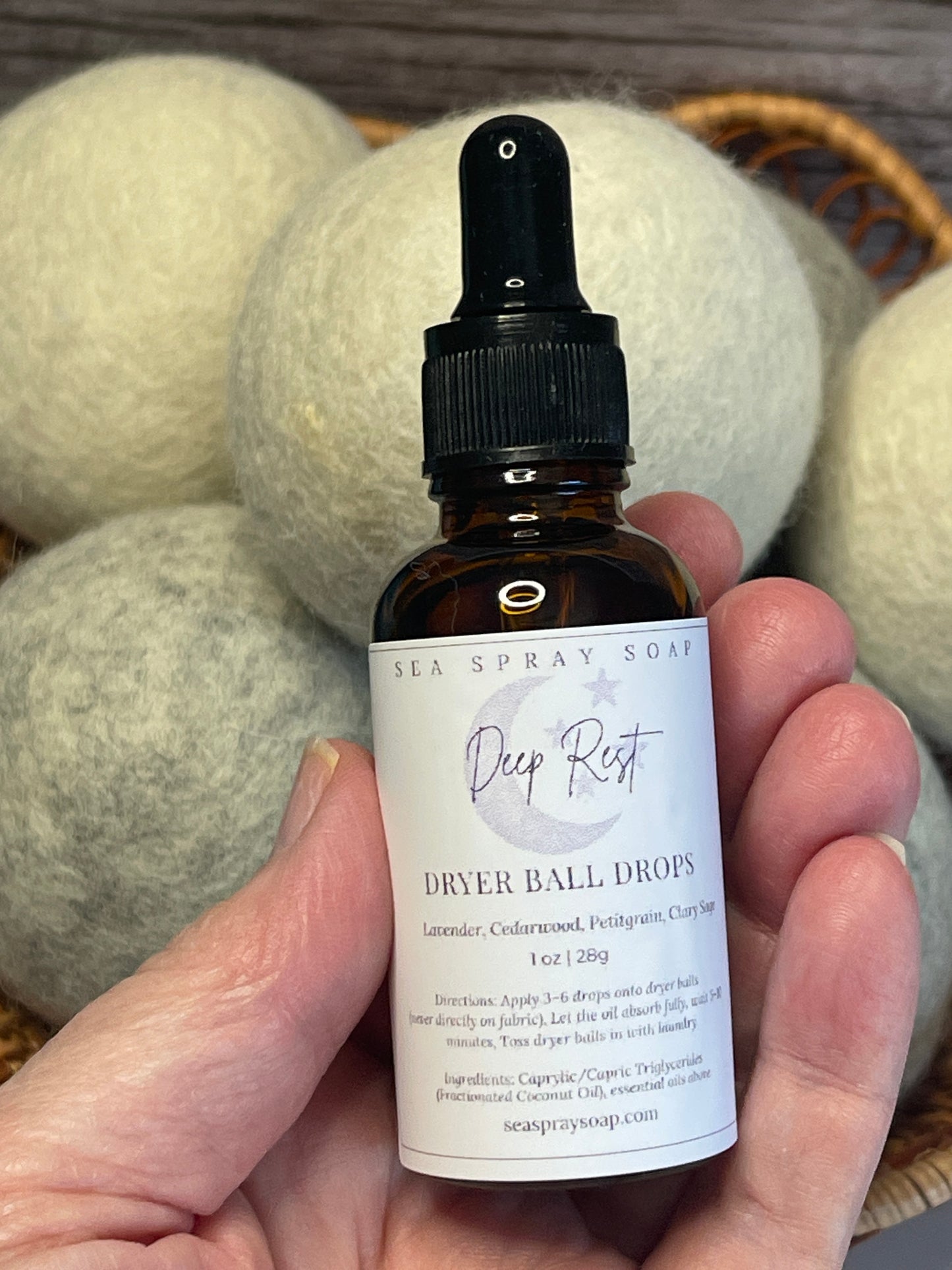 Hand holding a bottle labeled 'Deep Rest' with dryer balls in the background