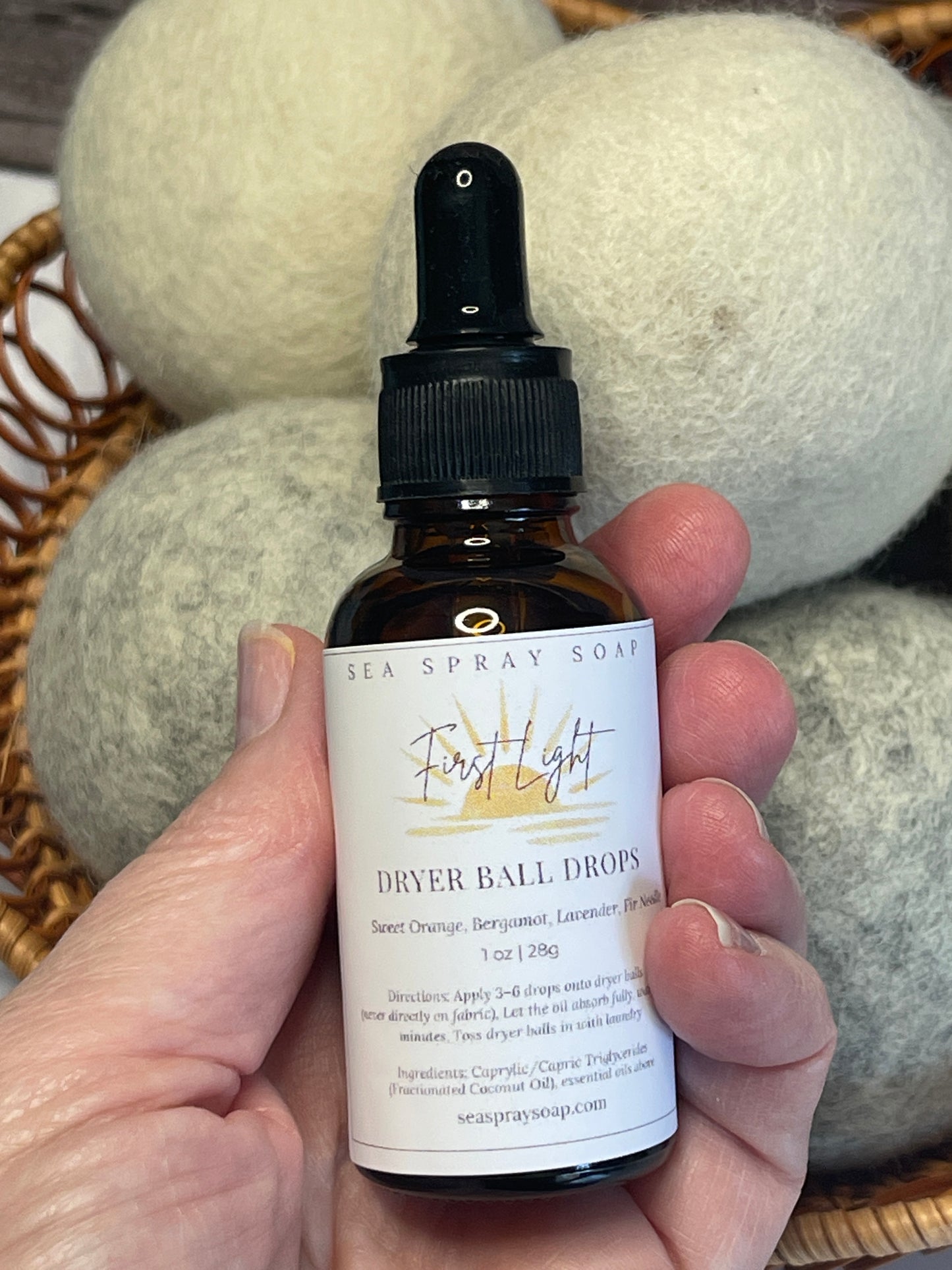 Hand holding a bottle of dryer ball drops with a label, against a neutral background.